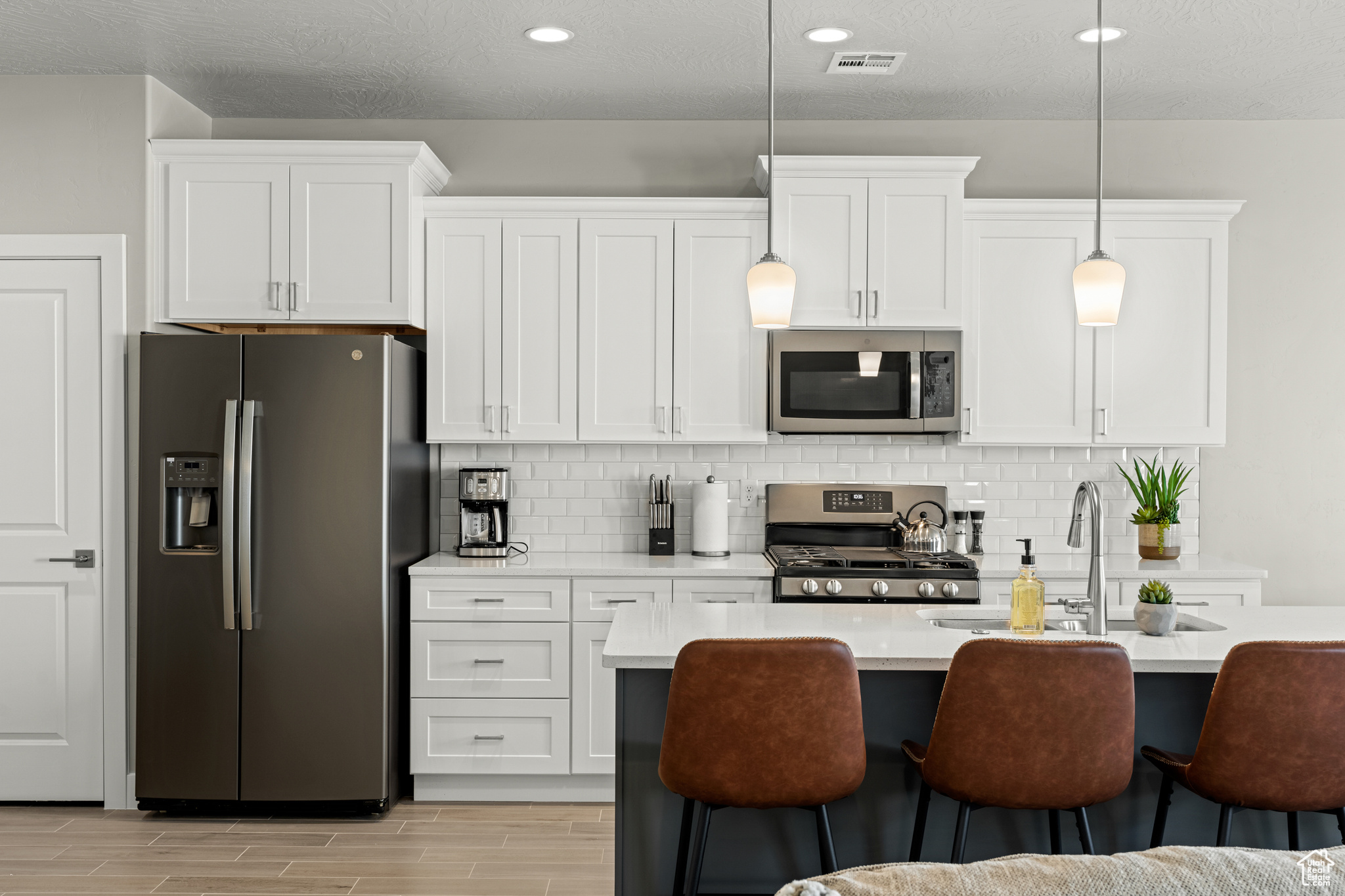 Kitchen featuring stainless steel appliances, white cabinets, and decorative light fixtures