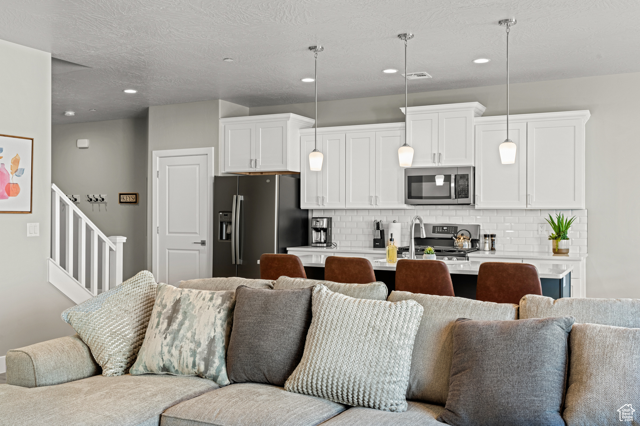 Kitchen featuring hanging light fixtures, white cabinets, stainless steel appliances, tasteful backsplash, and an island with sink