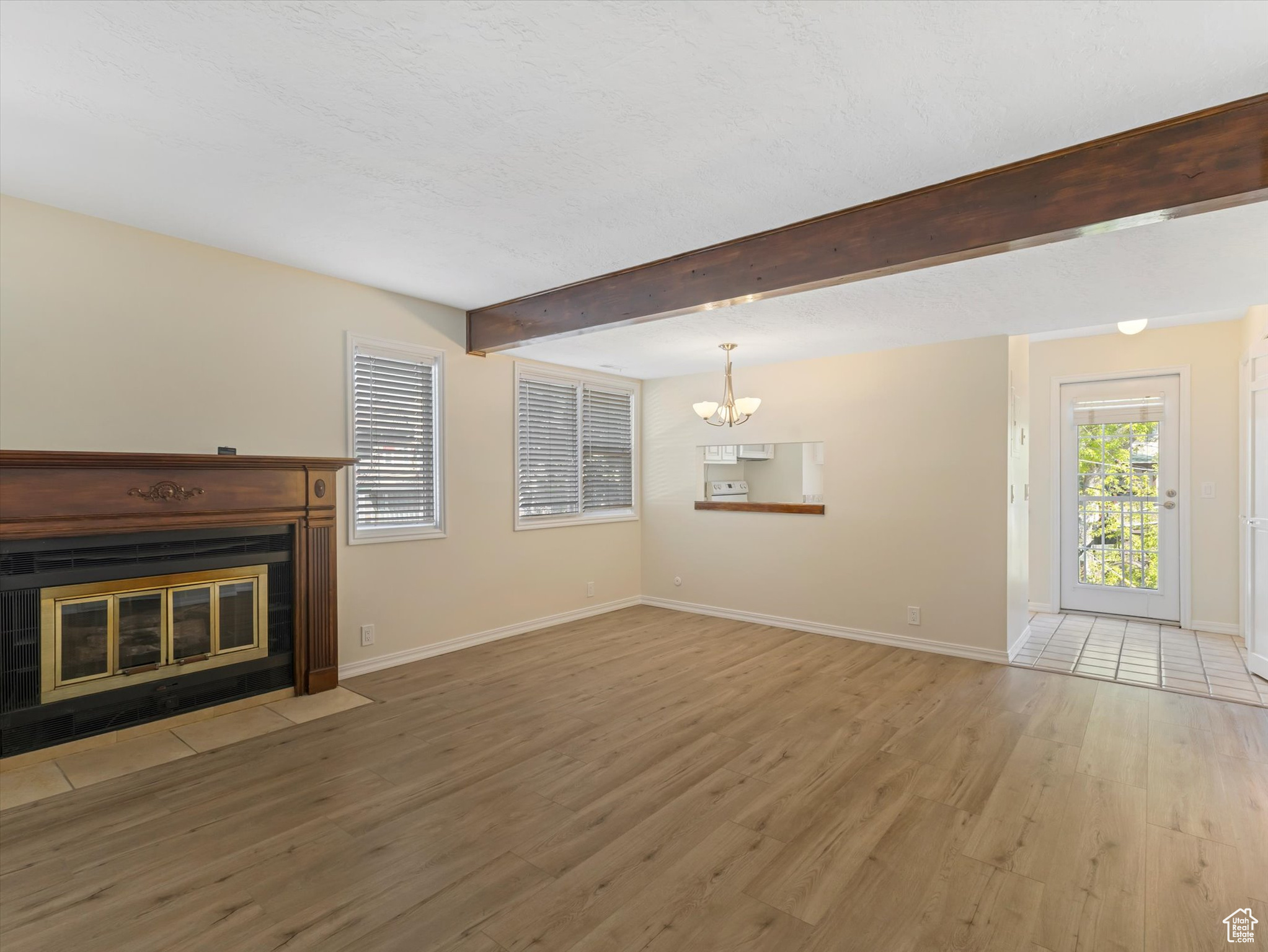 Unfurnished living room featuring hardwood / wood-style floors, beam ceiling, and a chandelier
