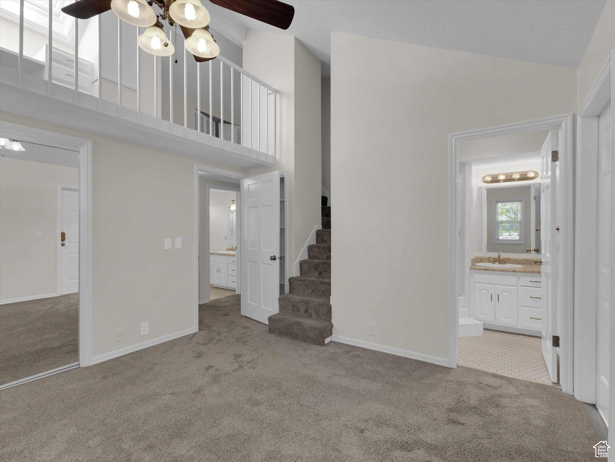 Interior space featuring high vaulted ceiling, ensuite bathroom, sink, light colored carpet, and ceiling fan