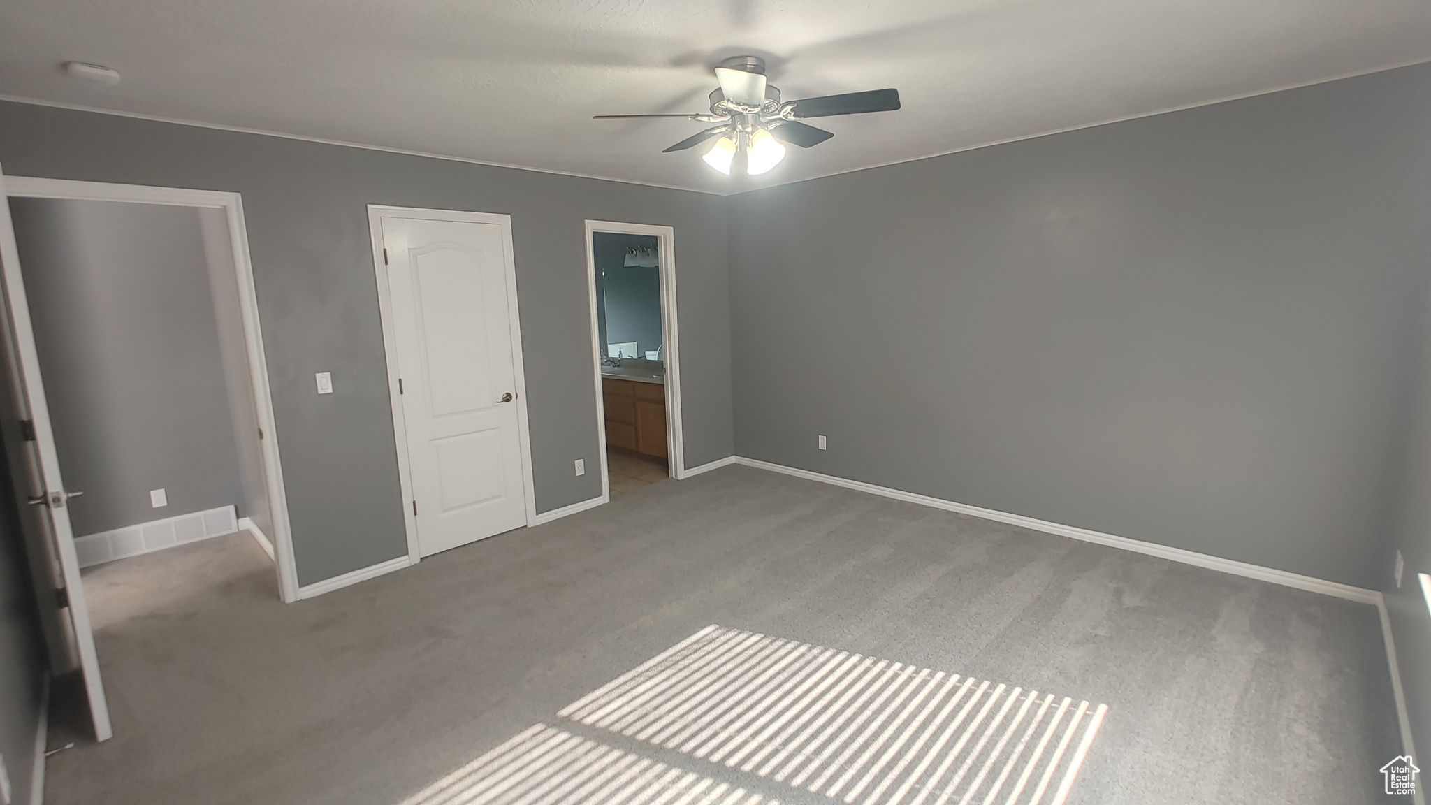 Unfurnished bedroom with dark carpet, ceiling fan, and ensuite bathroom