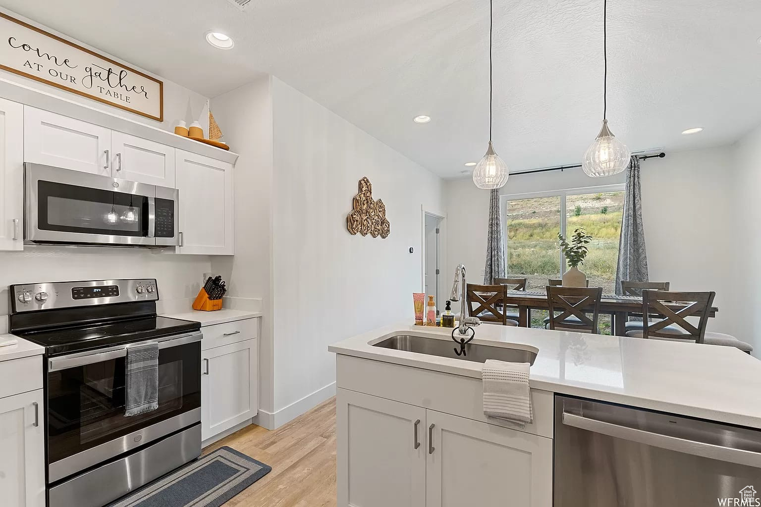 Kitchen with sink, white cabinetry, hanging light fixtures, stainless steel appliances, and light hardwood / wood-style flooring