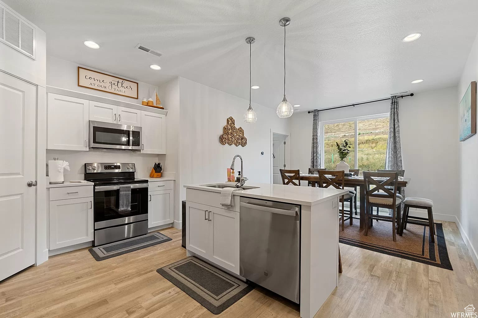 Kitchen with stainless steel appliances, white cabinetry, sink, and light wood-type flooring