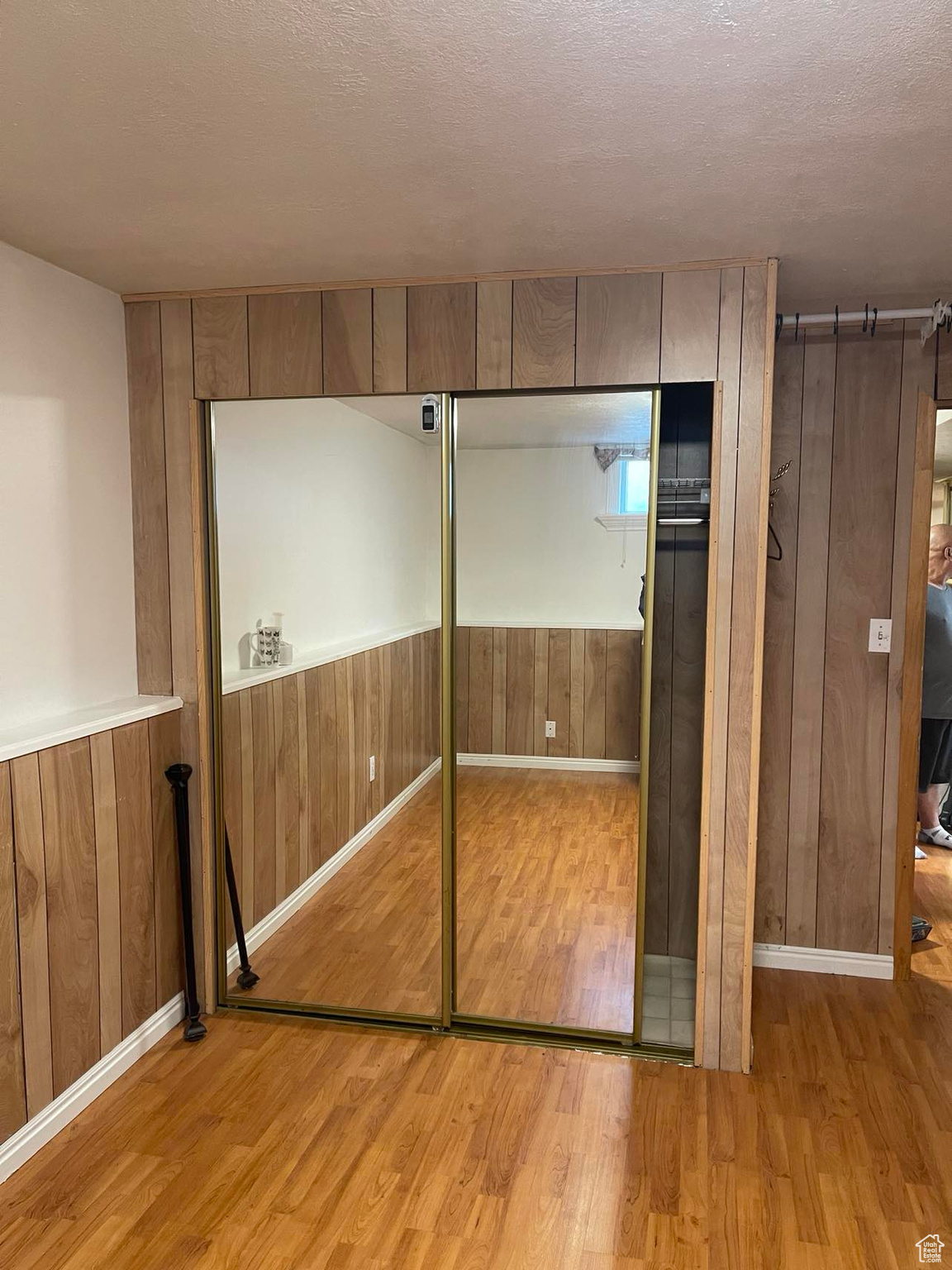 Unfurnished bedroom with wood walls, a barn door, light hardwood / wood-style flooring, a textured ceiling, and a closet