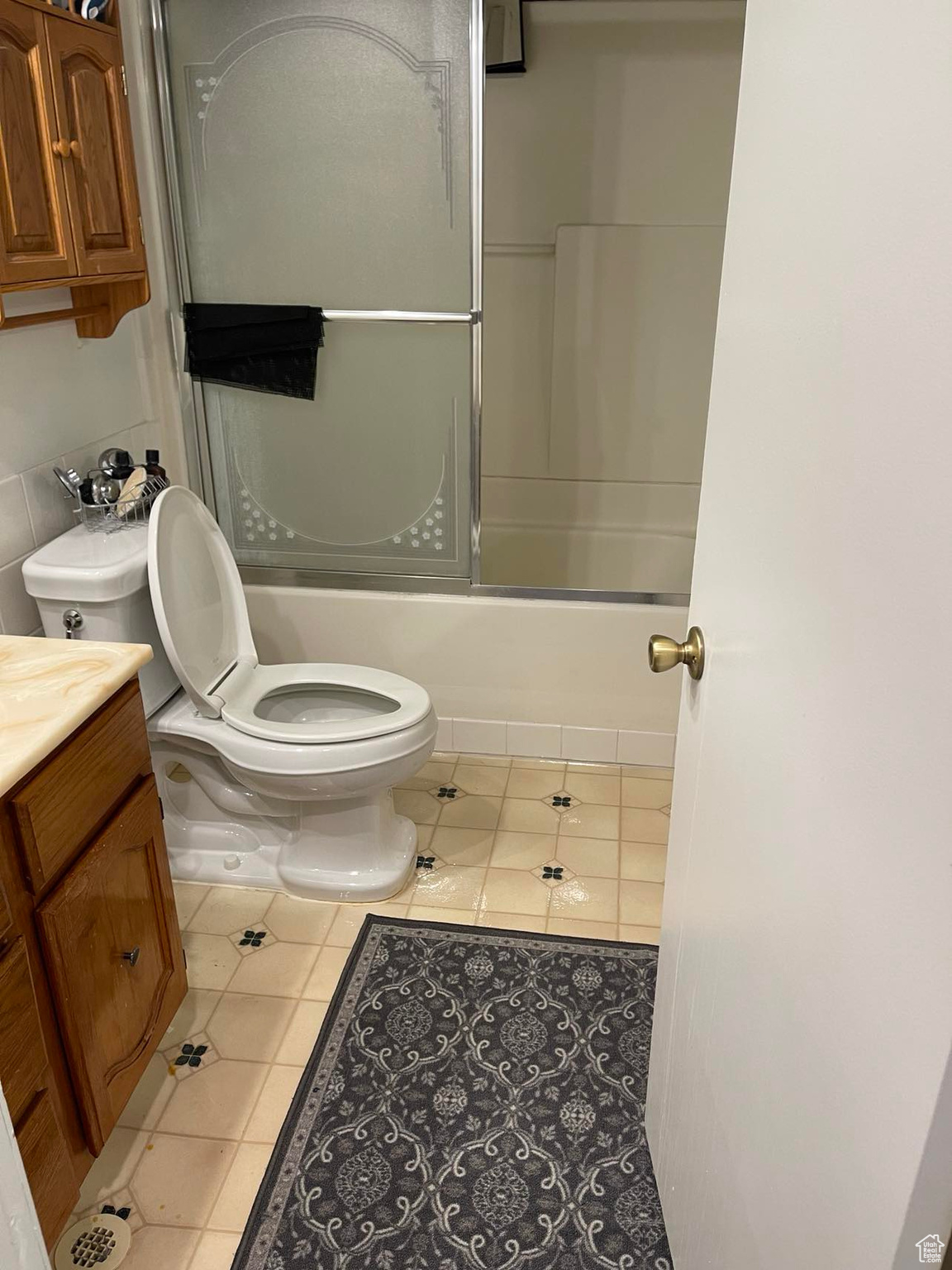 Full bathroom with vanity, tile floors, toilet, and bath / shower combo with glass door