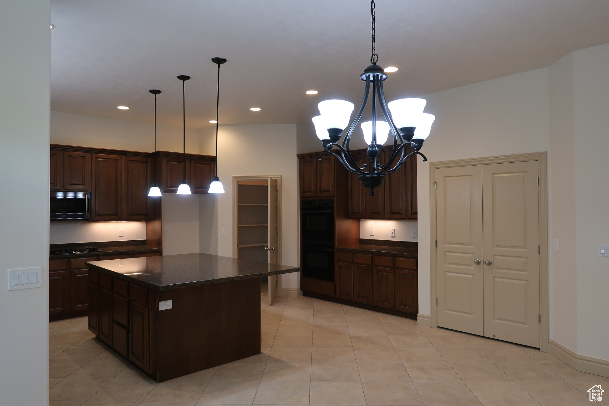 Kitchen with a center island, pendant lighting, black double oven, a notable chandelier, and light tile floors