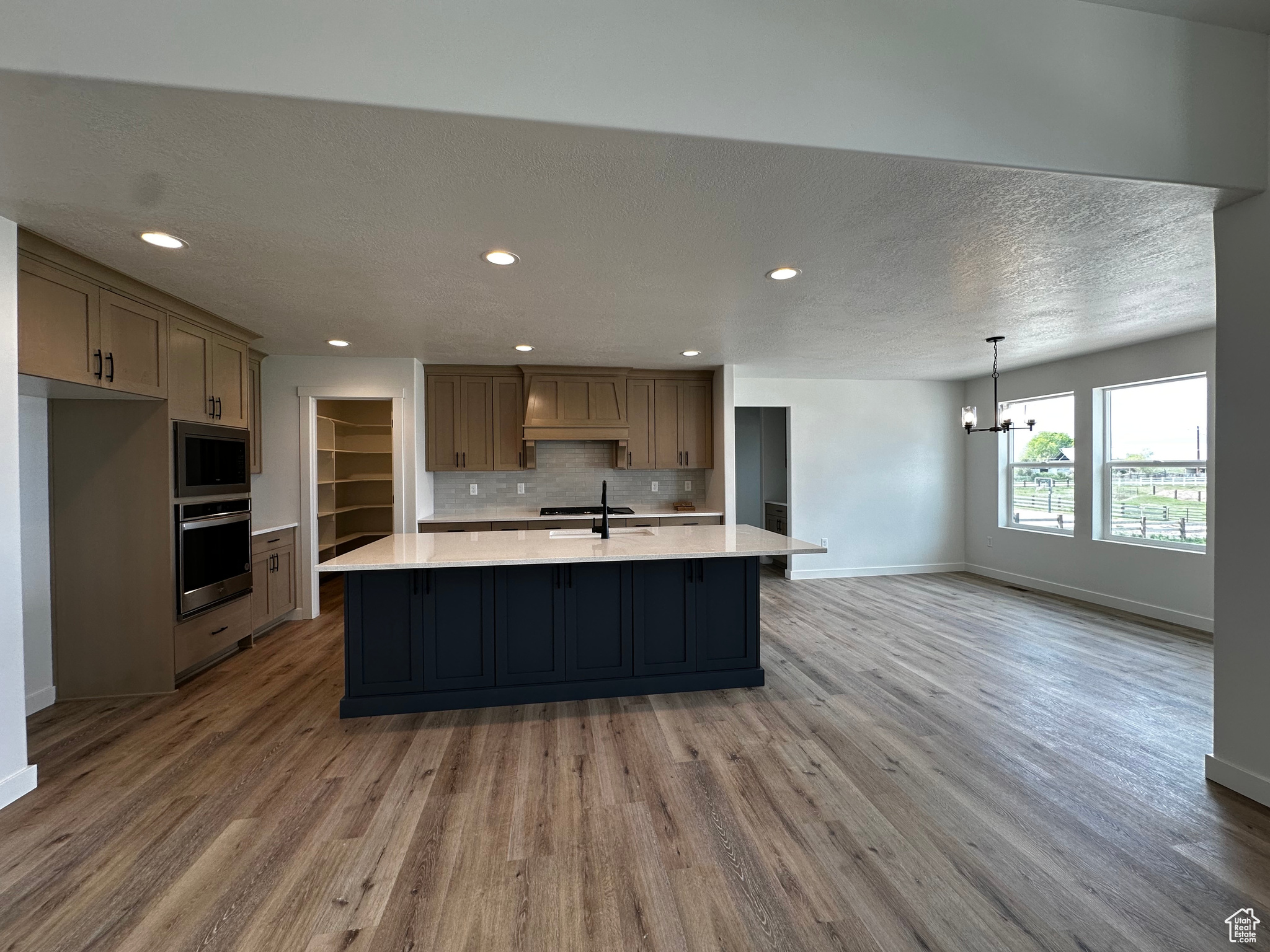 Kitchen featuring premium range hood, hardwood / wood-style floors, stainless steel microwave, tasteful backsplash, and an island with sink