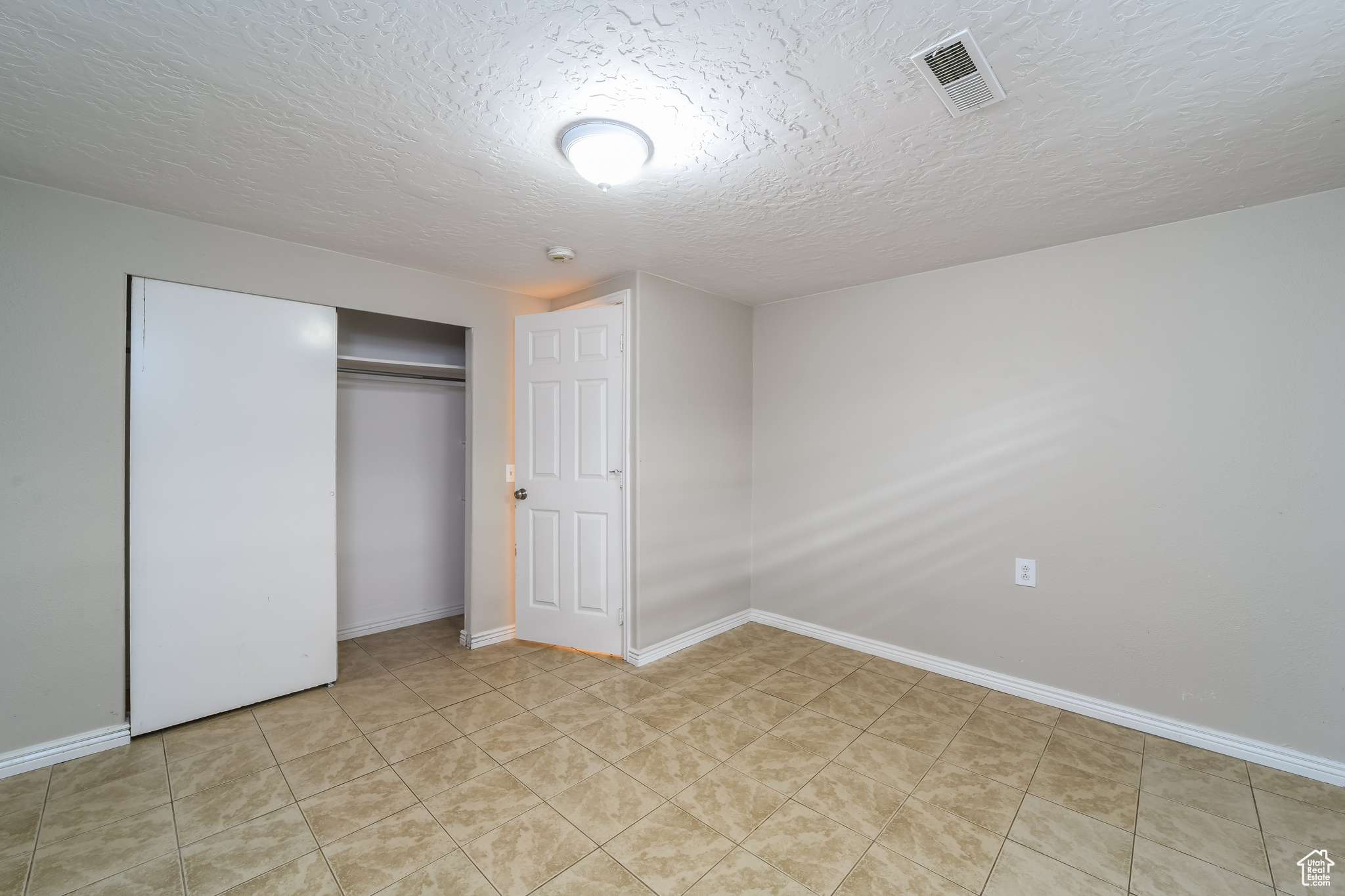 Unfurnished bedroom featuring a closet, light tile floors, and a textured ceiling