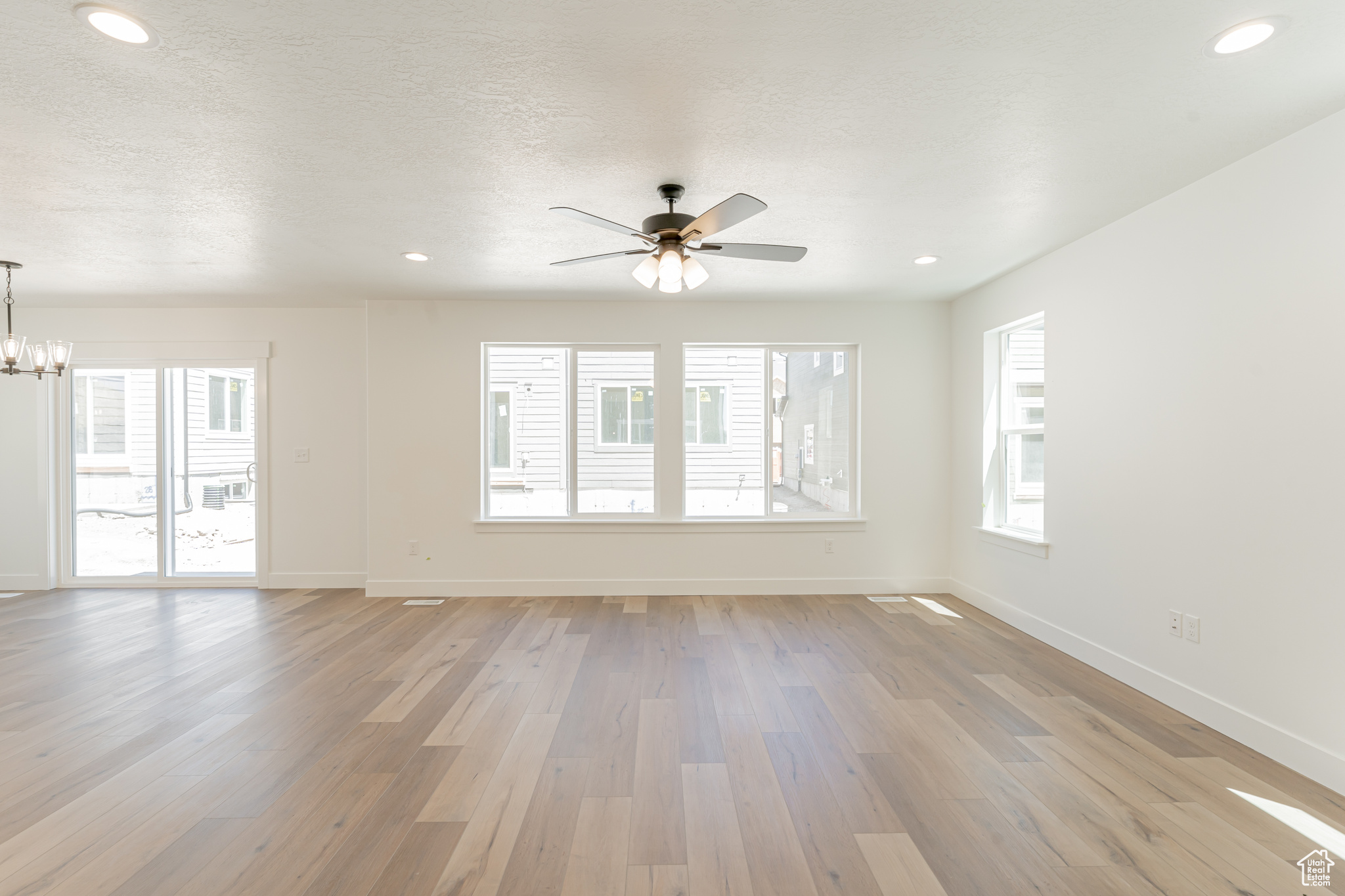 Interior space with ceiling fan with notable chandelier, light hardwood / wood-style flooring, and a textured ceiling