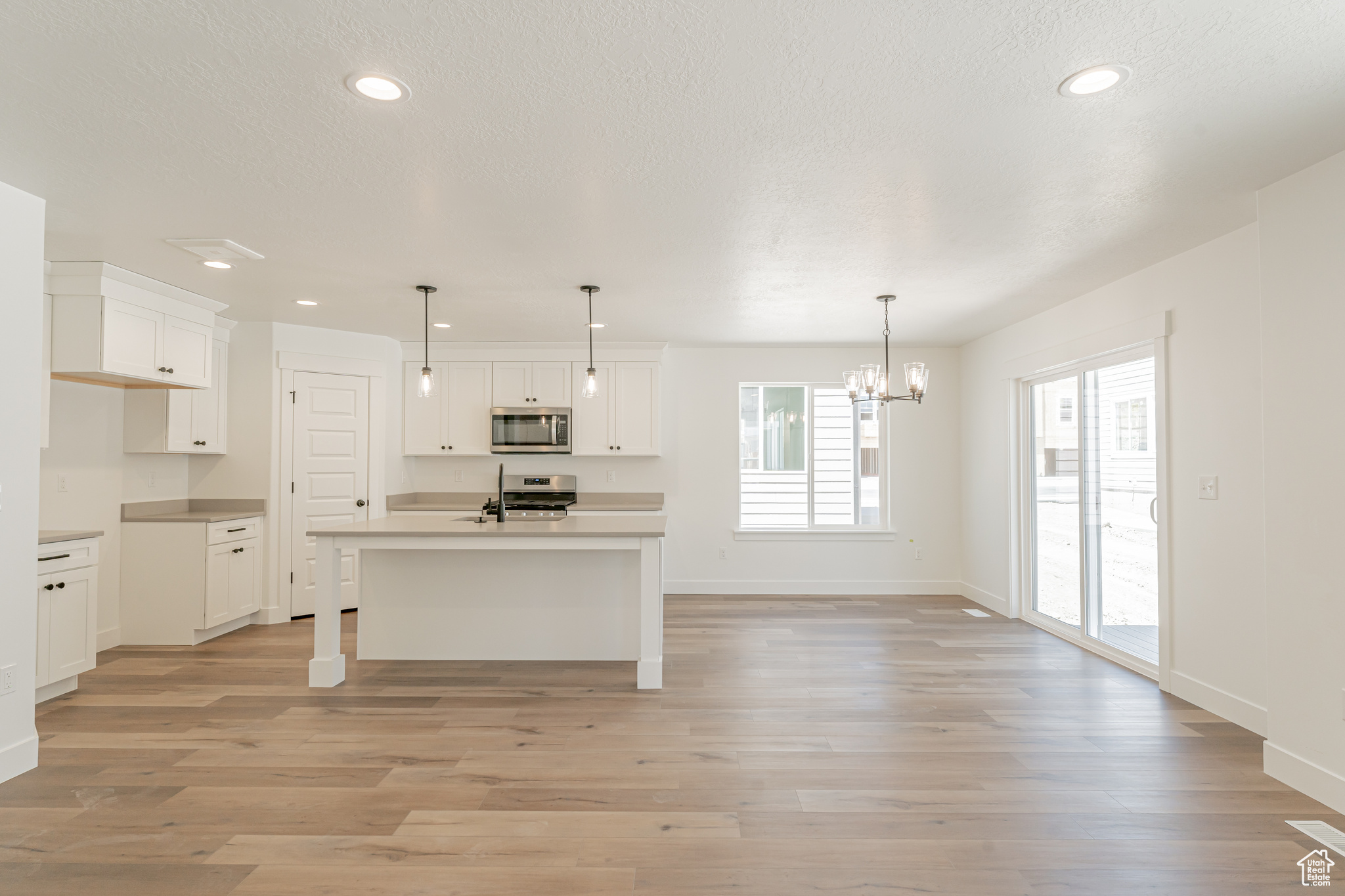 Kitchen featuring hanging light fixtures, light hardwood / wood-style flooring, white cabinetry, and an island with sink