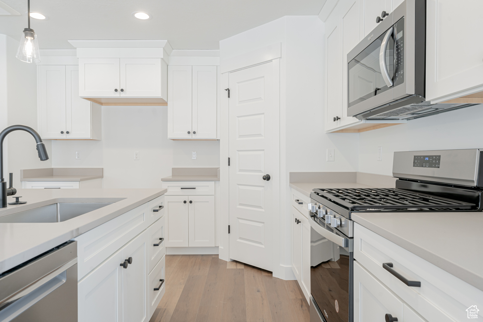 Kitchen with sink, light hardwood / wood-style flooring, white cabinets, and stainless steel appliances