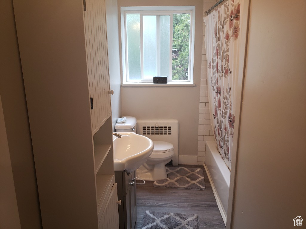 Full bathroom with radiator, shower / bath combo, toilet, vanity, and hardwood / wood-style floors
