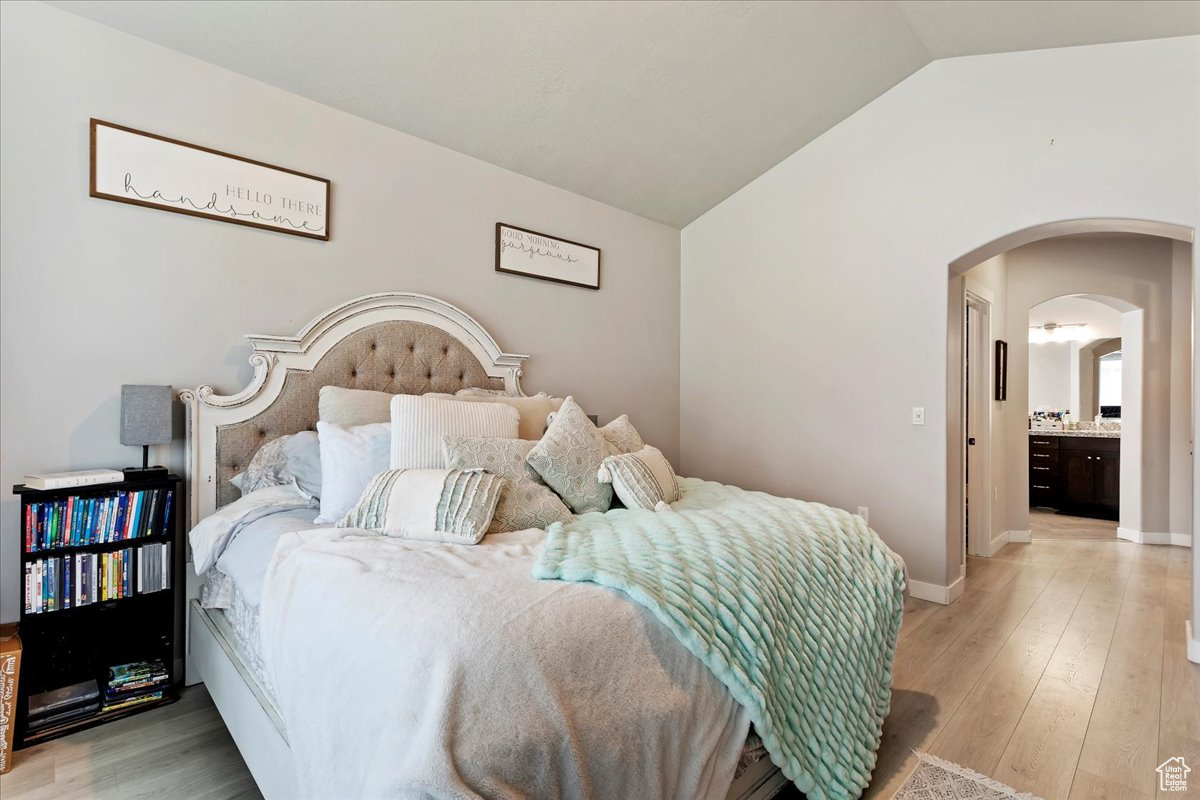 Bedroom with light hardwood / wood-style flooring, vaulted ceiling, and ensuite bathroom