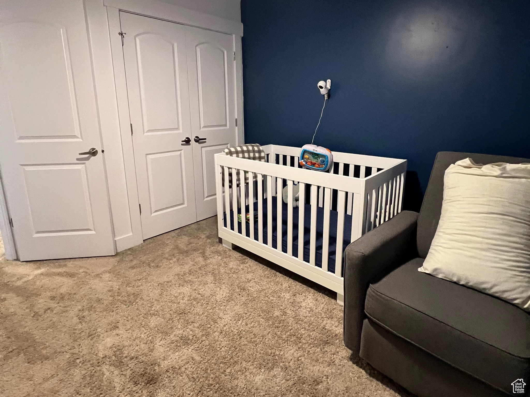 Carpeted bedroom with a closet, ceiling fan, and a nursery area