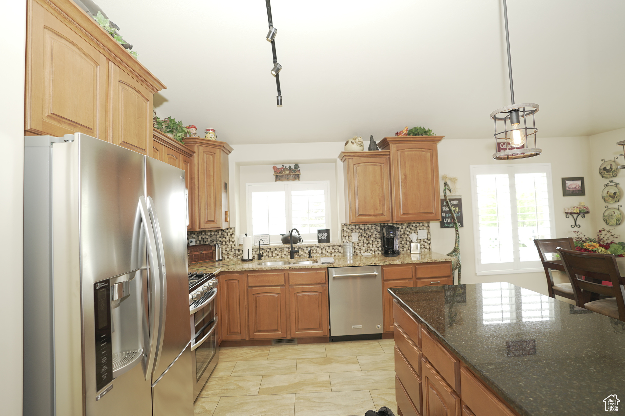 Kitchen featuring decorative light fixtures, backsplash, stainless steel appliances, sink, and light tile floors