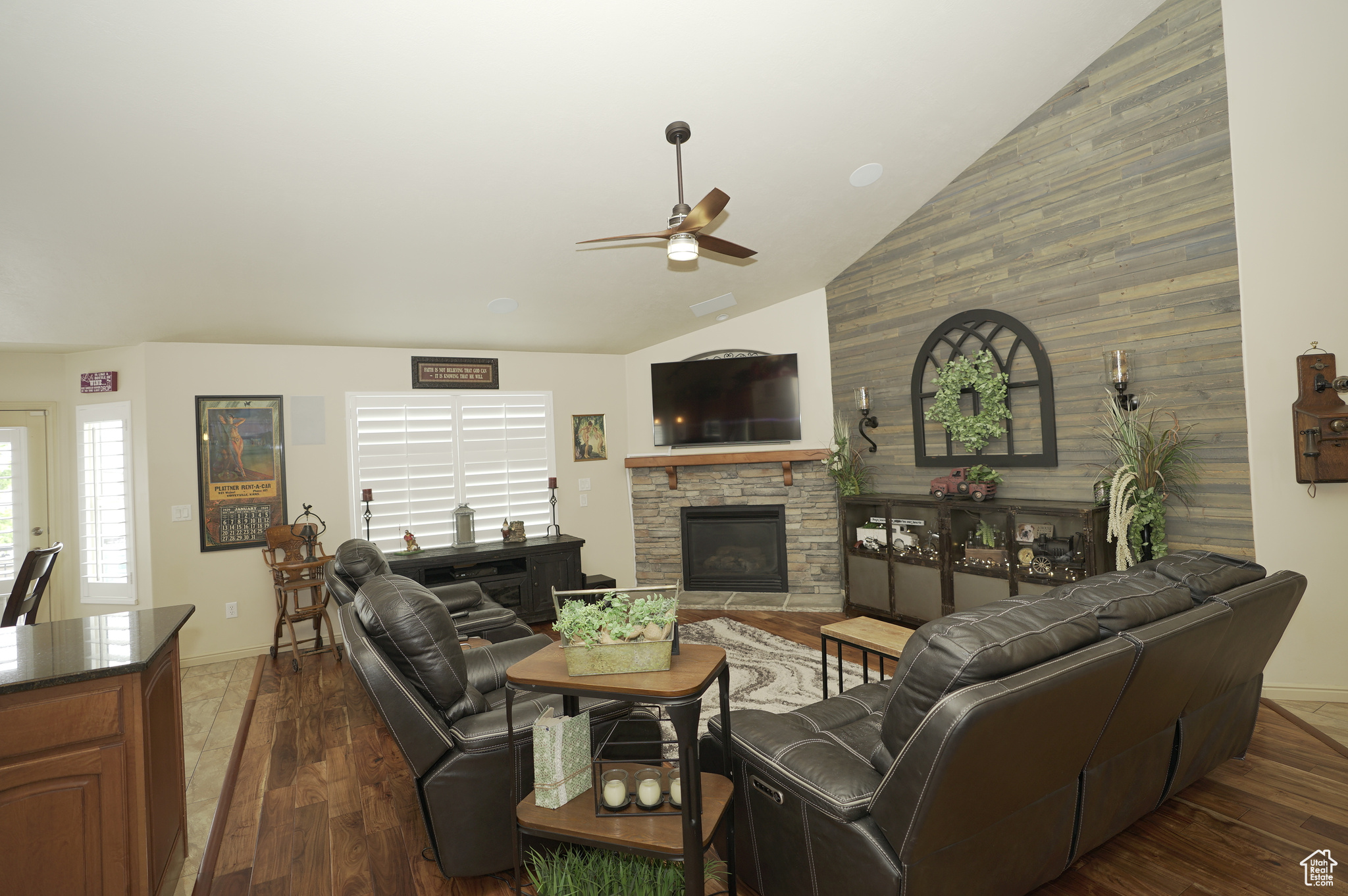 Living room with wood walls, ceiling fan, a fireplace, and lofted ceiling
