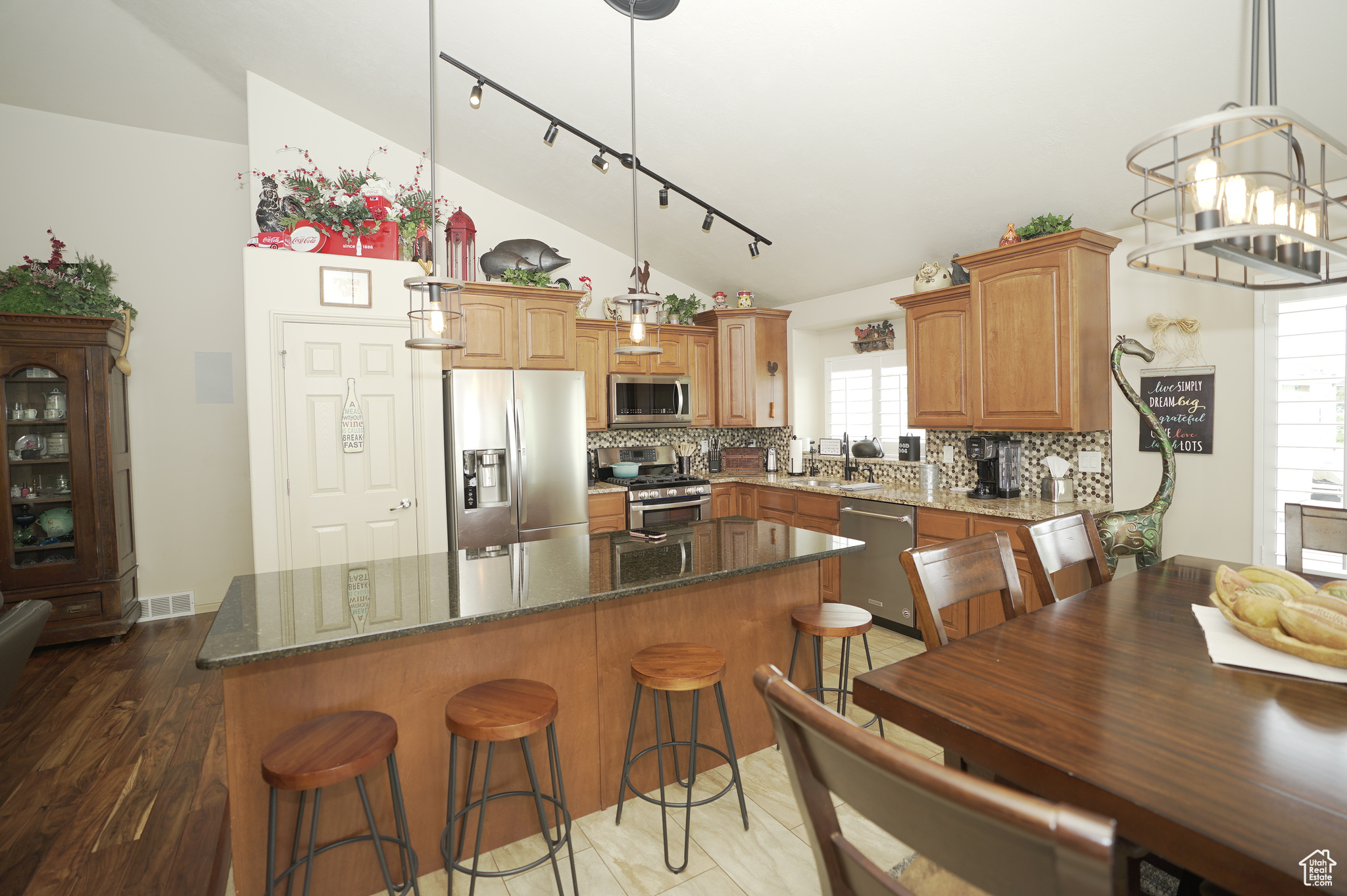 Kitchen featuring rail lighting, backsplash, stainless steel appliances, sink, and lofted ceiling