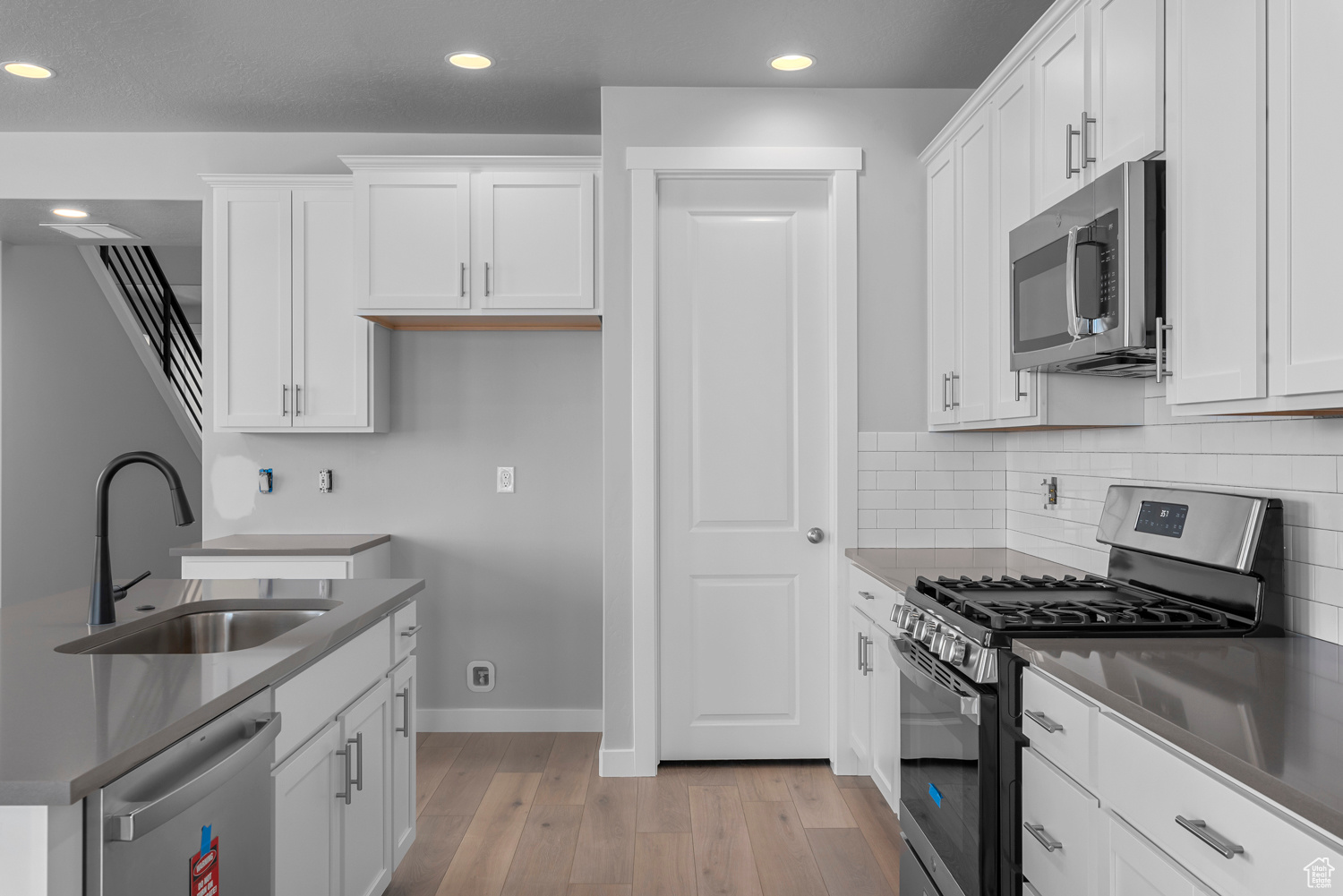 Kitchen featuring white cabinets, stainless steel appliances, tasteful backsplash, light wood-type flooring, and sink