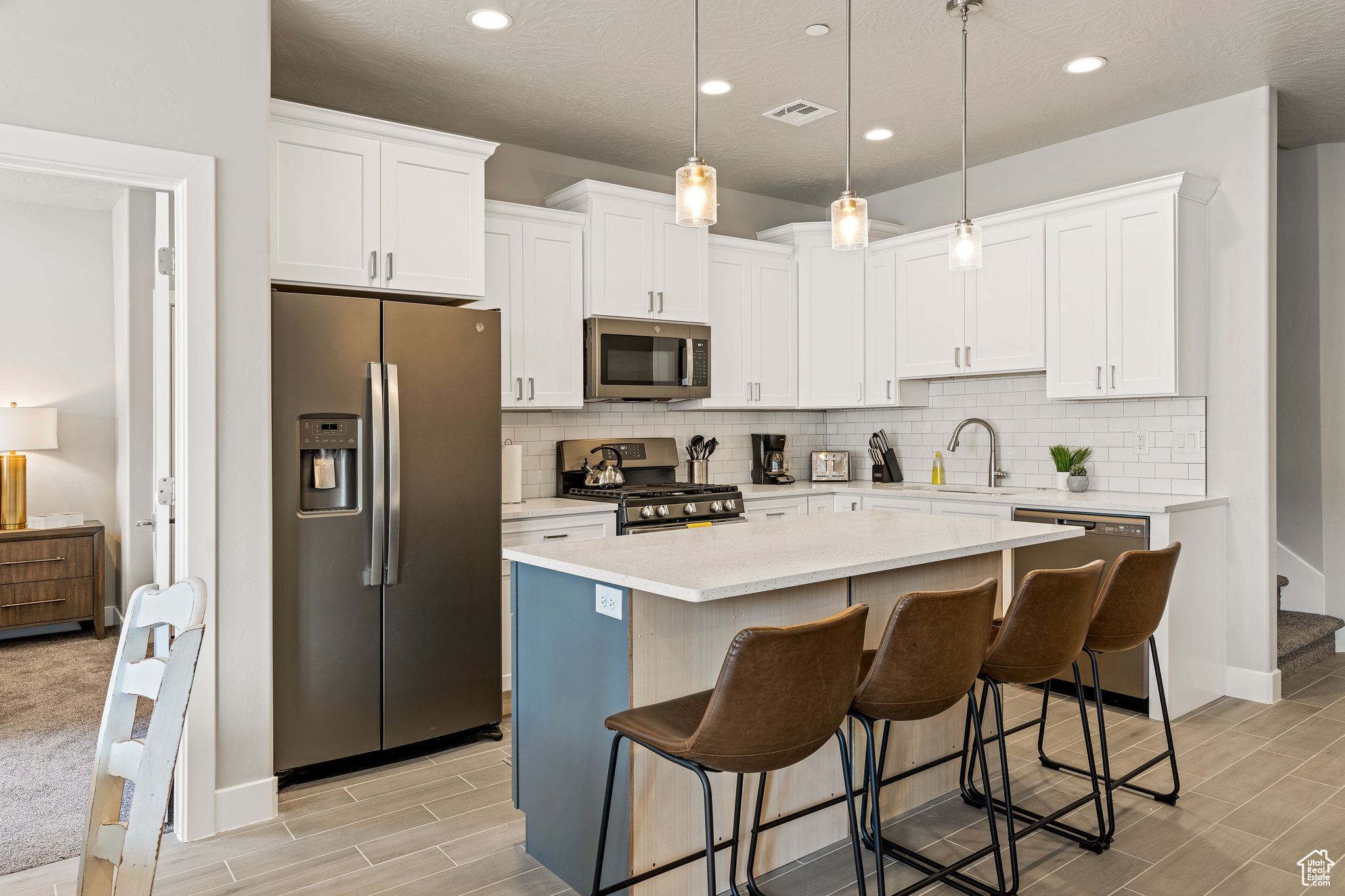 Kitchen featuring light colored carpet, hanging light fixtures, stainless steel appliances, a kitchen breakfast bar, and a center island