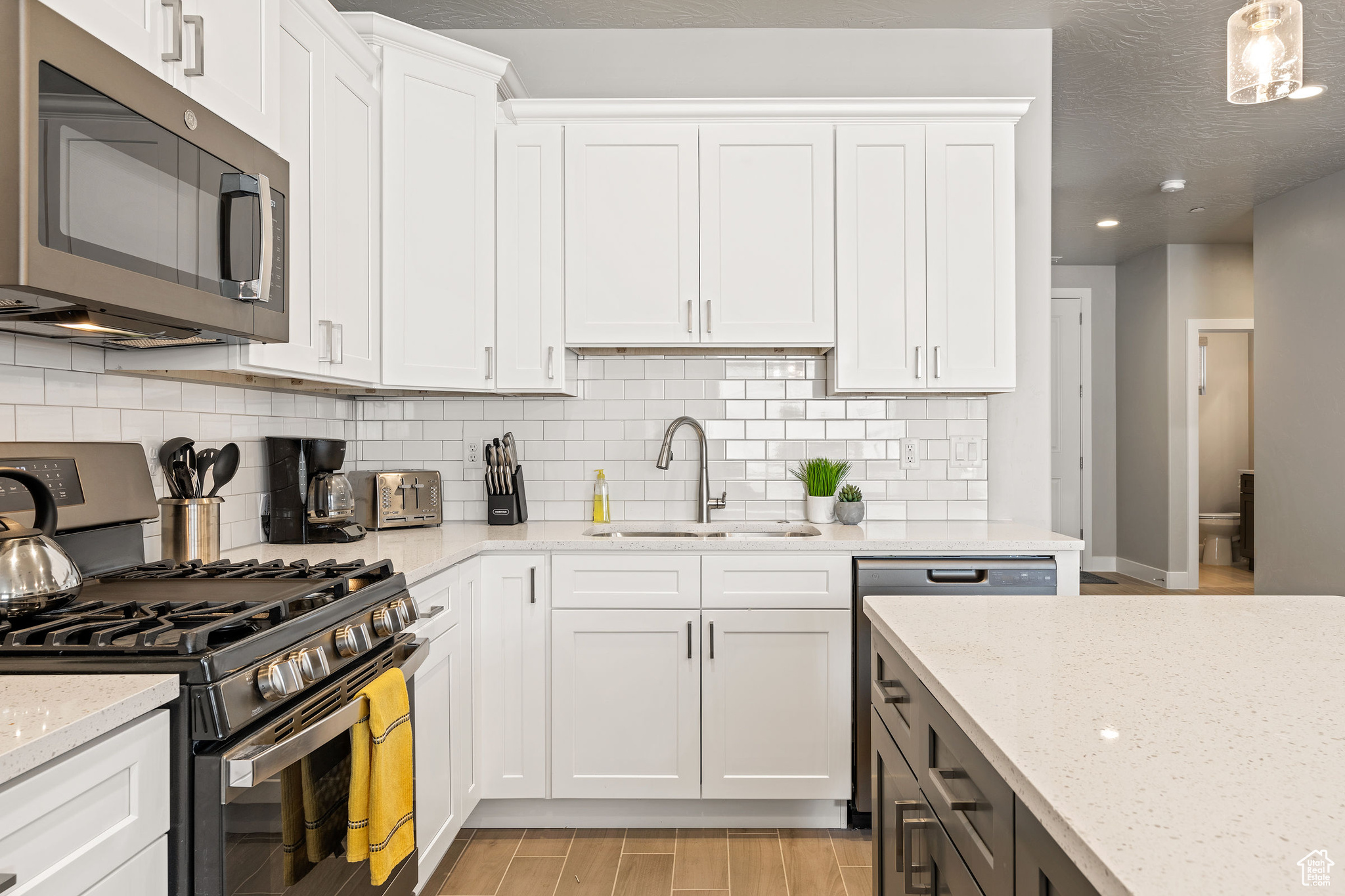 Kitchen with white cabinets, light hardwood / wood-style flooring, backsplash, appliances with stainless steel finishes, and sink