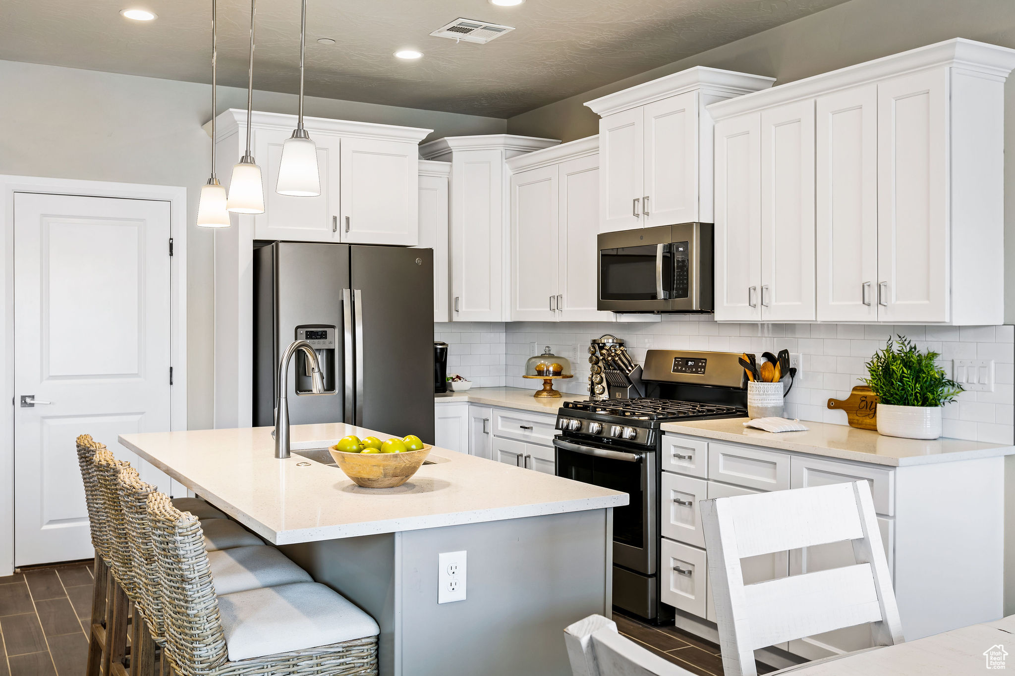 Kitchen featuring hanging light fixtures, stainless steel appliances, a center island with sink, tasteful backsplash, and white cabinets