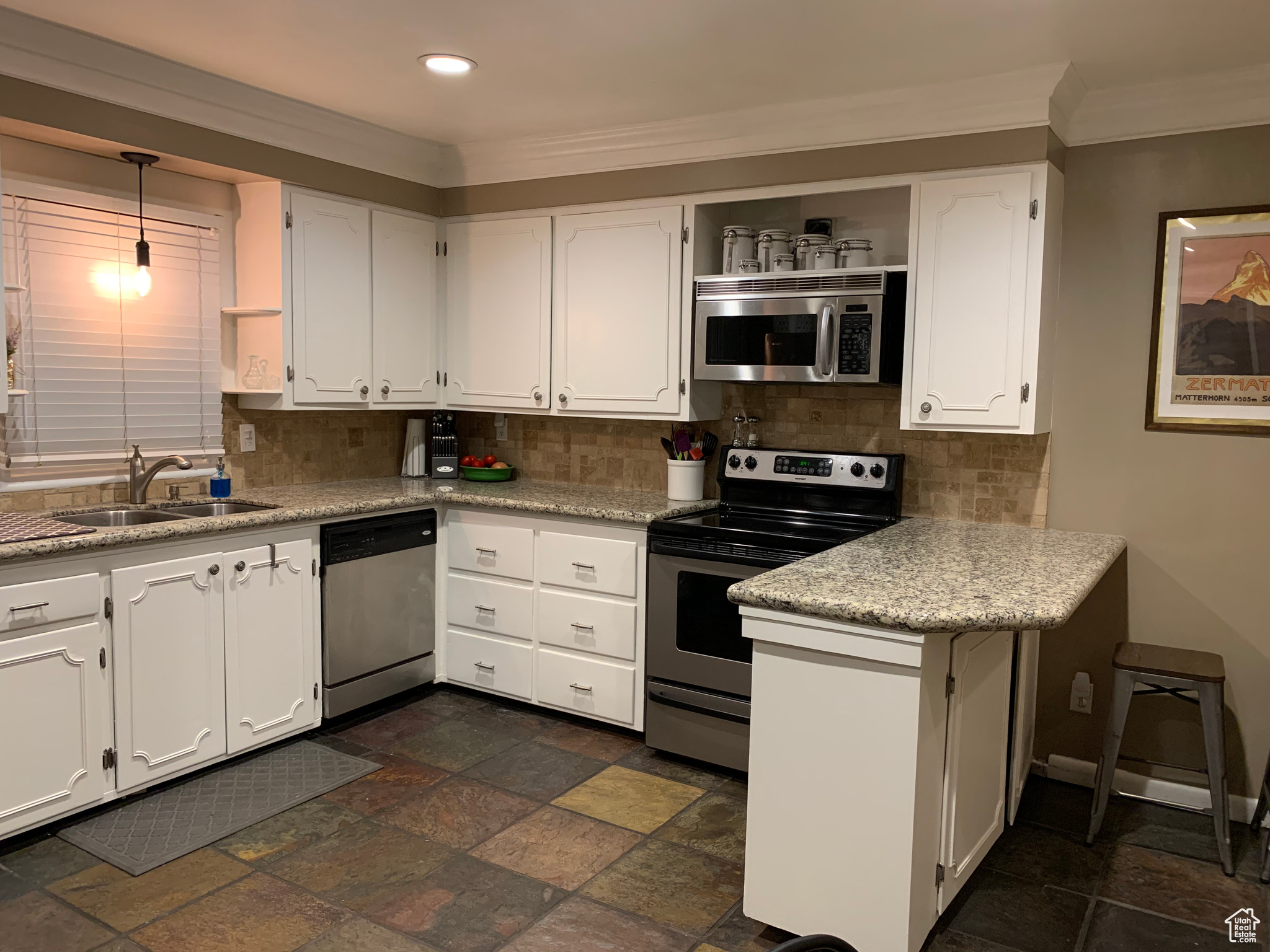 Kitchen featuring decorative light fixtures, appliances with stainless steel finishes, tasteful backsplash, white cabinets, and sink