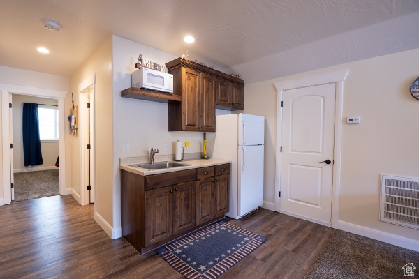 Kitchen with dark hardwood / wood-style floors, sink, dark brown cabinets, and white appliances