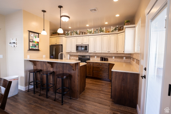 Kitchen featuring appliances with stainless steel finishes, tasteful backsplash, a breakfast bar area, dark wood-type flooring, and pendant lighting