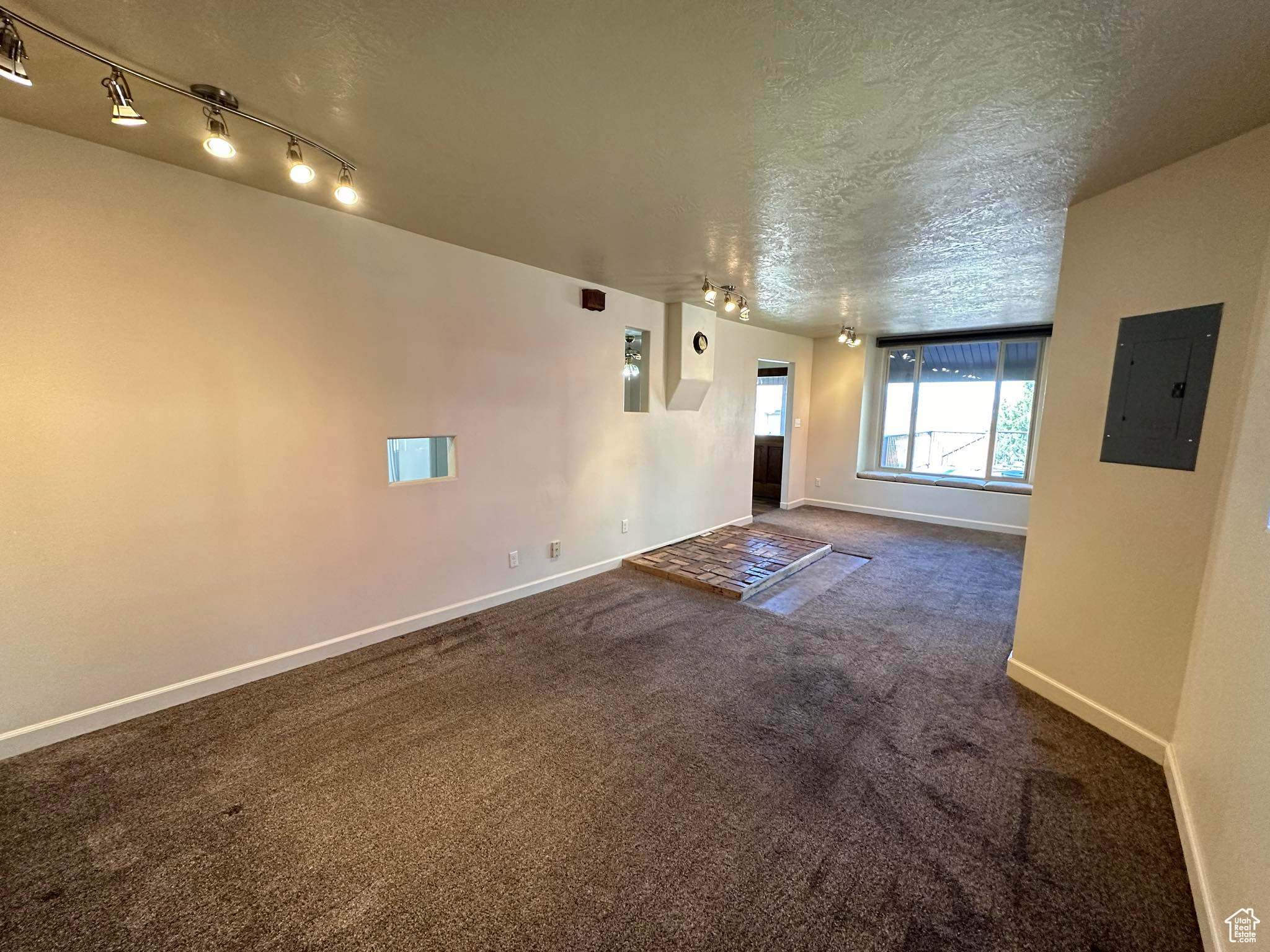 Spare room featuring a textured ceiling, track lighting, and dark colored carpet