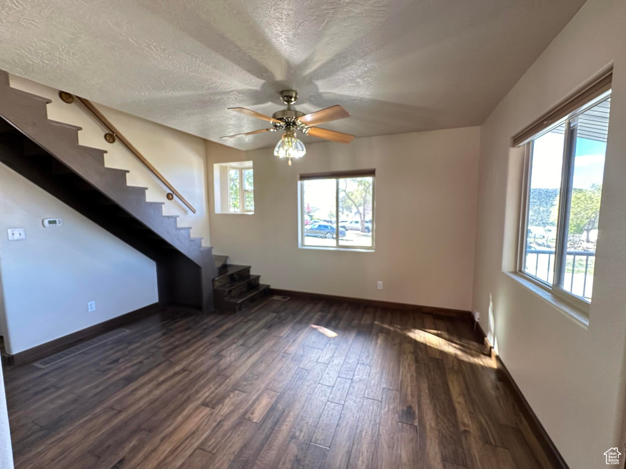 Spare room with a healthy amount of sunlight, ceiling fan, dark hardwood / wood-style floors, and a textured ceiling