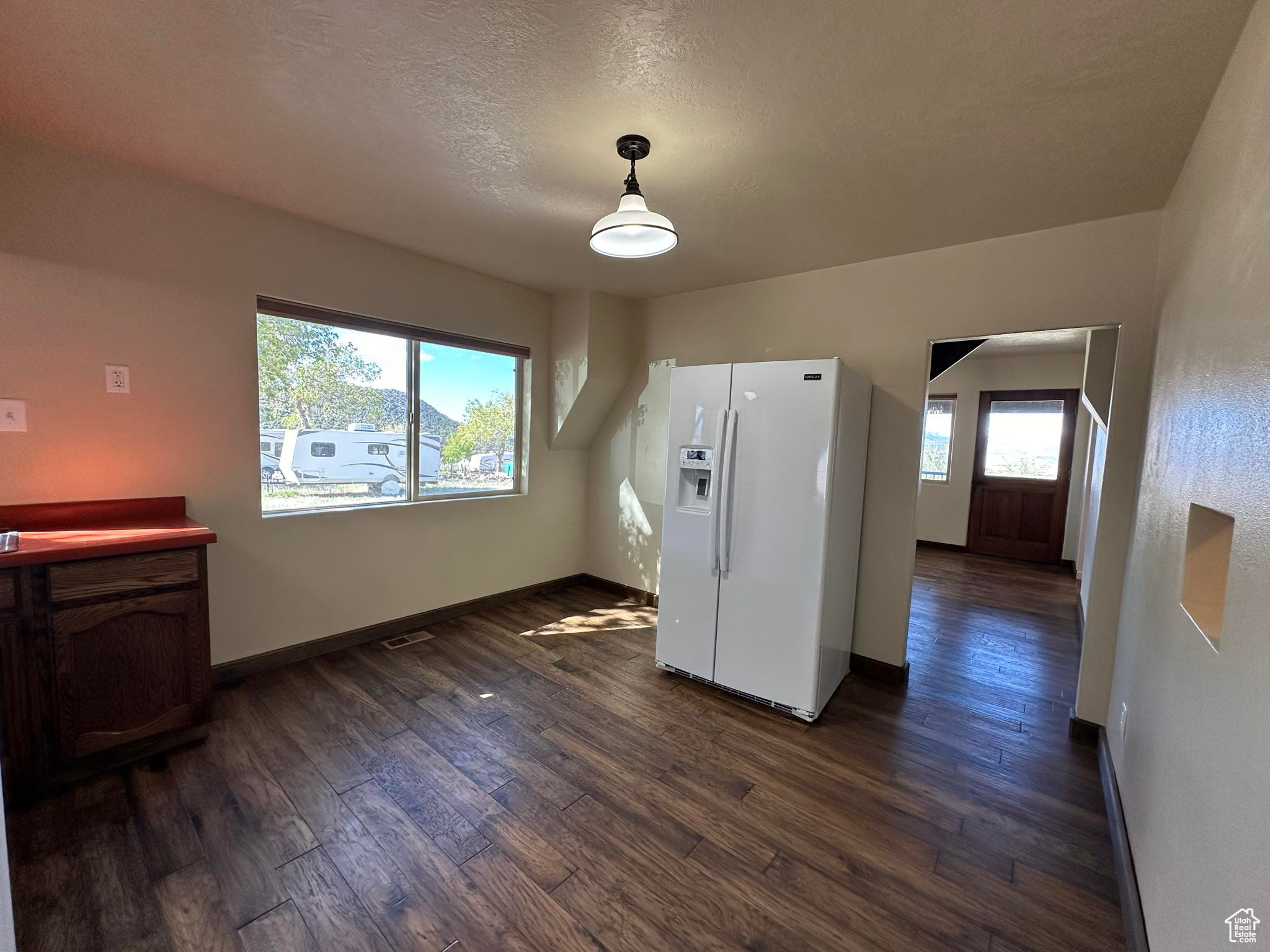 Kitchen with decorative light fixtures, white refrigerator with ice dispenser, dark hardwood / wood-style floors, and a textured ceiling