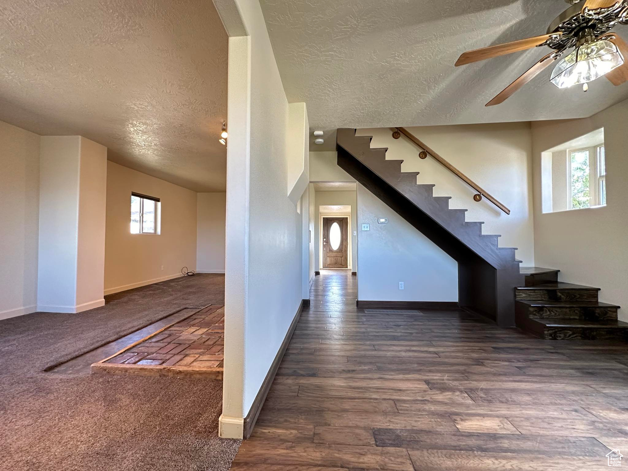 Unfurnished living room with a textured ceiling, ceiling fan, and dark colored carpet