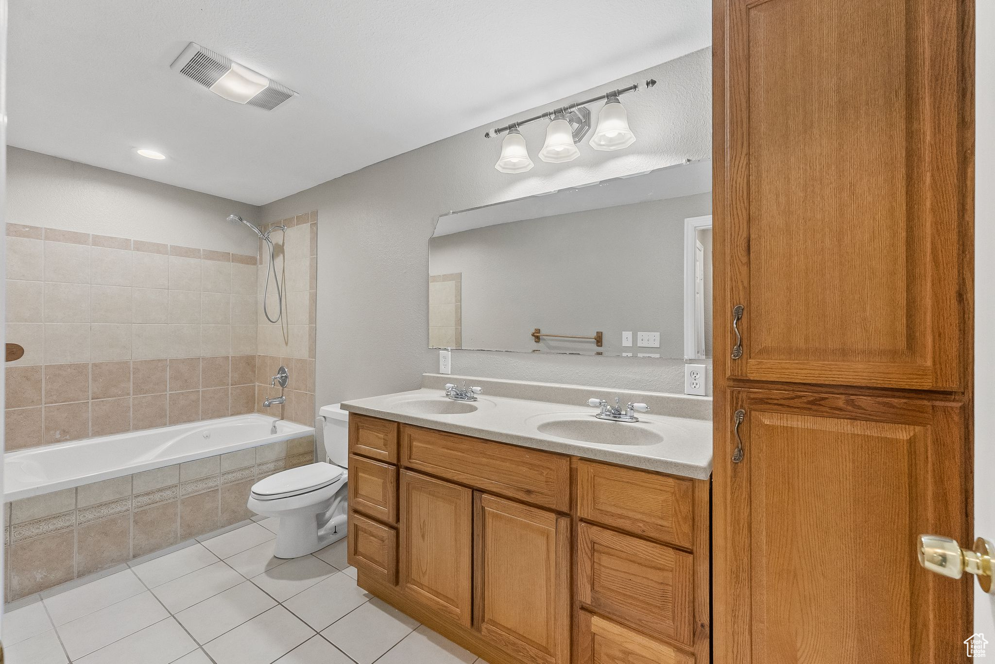 Full bathroom with tiled shower / bath, toilet, tile floors, and double sink vanity