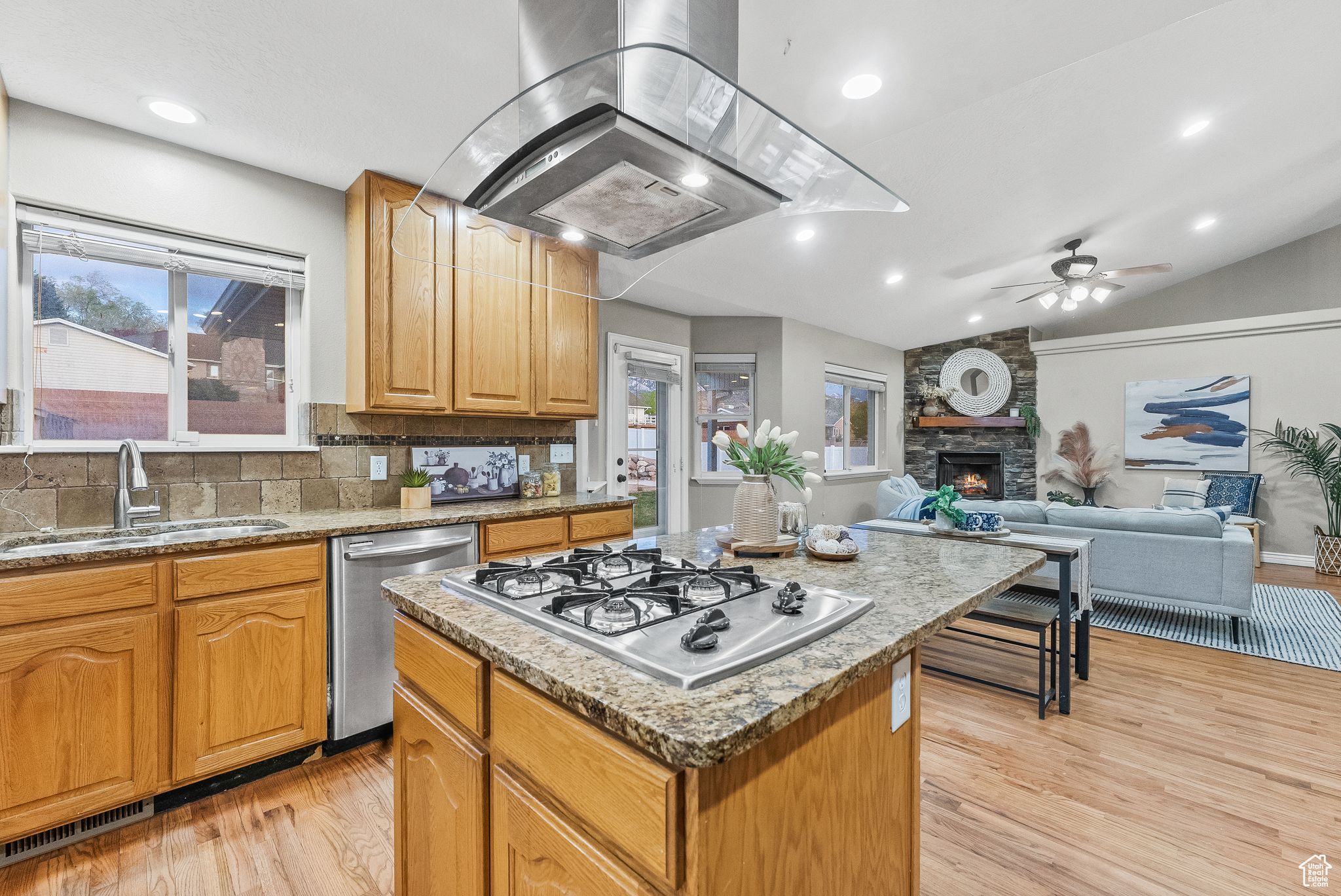 Kitchen featuring light hardwood / wood-style flooring, island range hood, backsplash, a kitchen island, and a stone fireplace