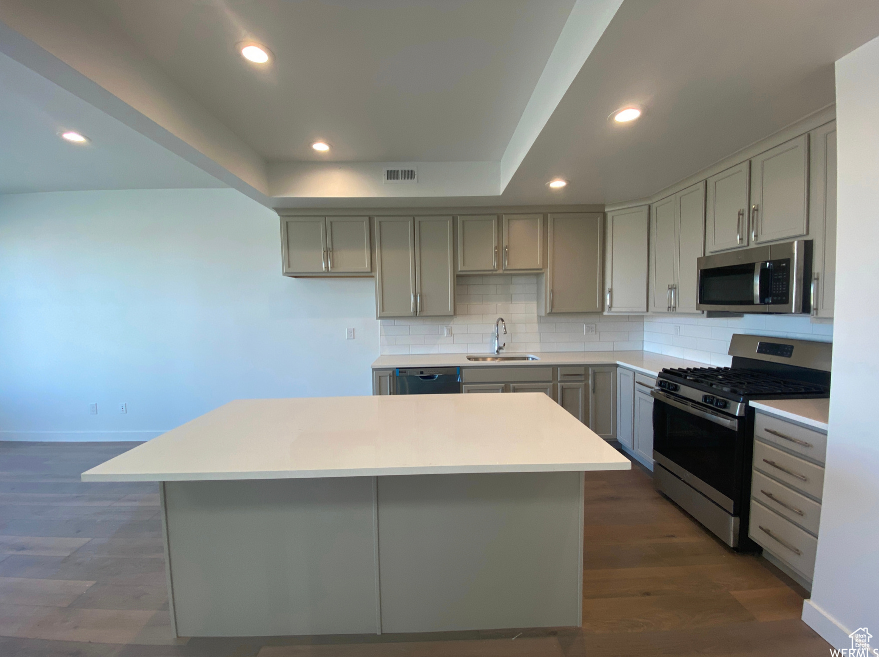 (previously built home as example) featuring appliances with stainless steel finishes, a center island, sink, backsplash, and dark hardwood / wood-style flooring