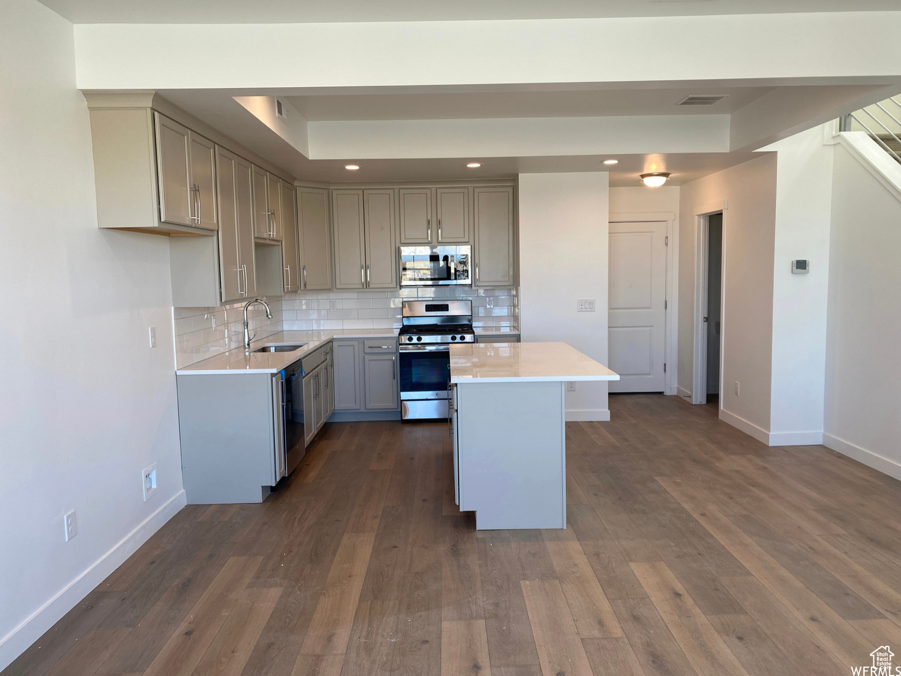 (previously built home as example) kitchen with appliances with stainless steel finishes, a center island, sink, tasteful backsplash, and dark wood-type flooring