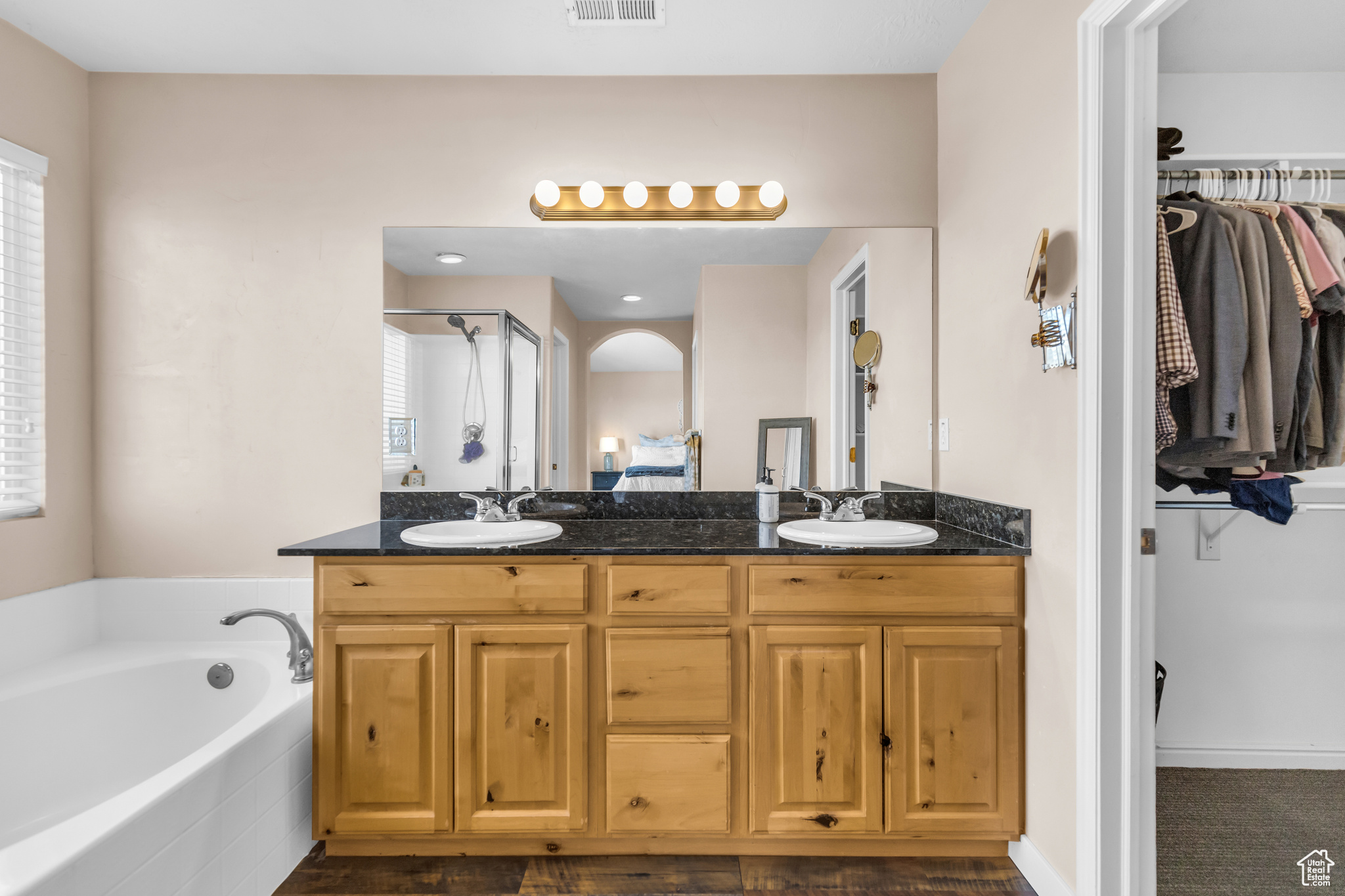 Bathroom with dual sinks, a wealth of natural light, tiled bath, and large vanity