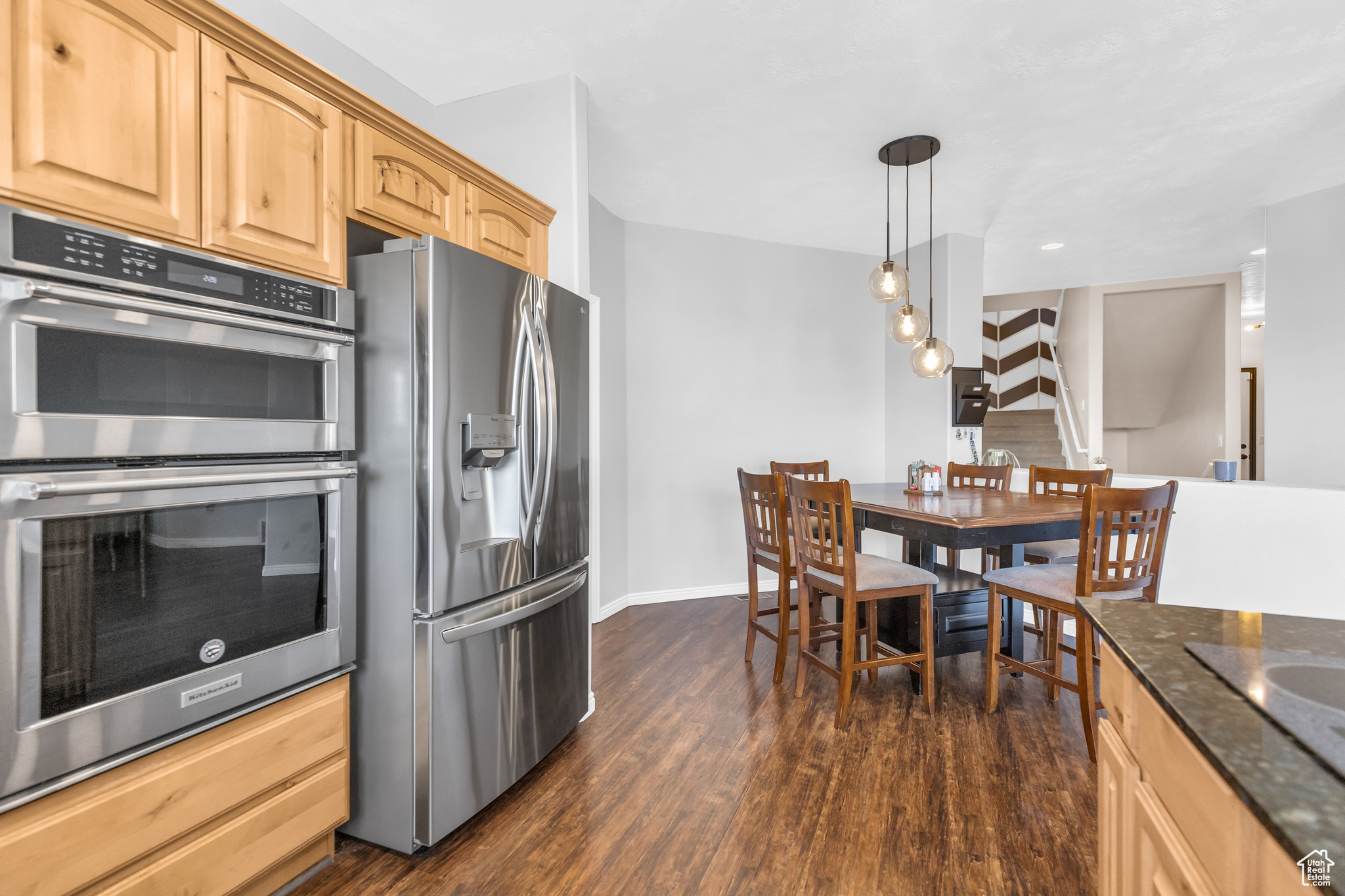 Kitchen featuring appliances with stainless steel finishes, dark hardwood / wood-style floors, dark stone countertops, light brown cabinetry, and pendant lighting