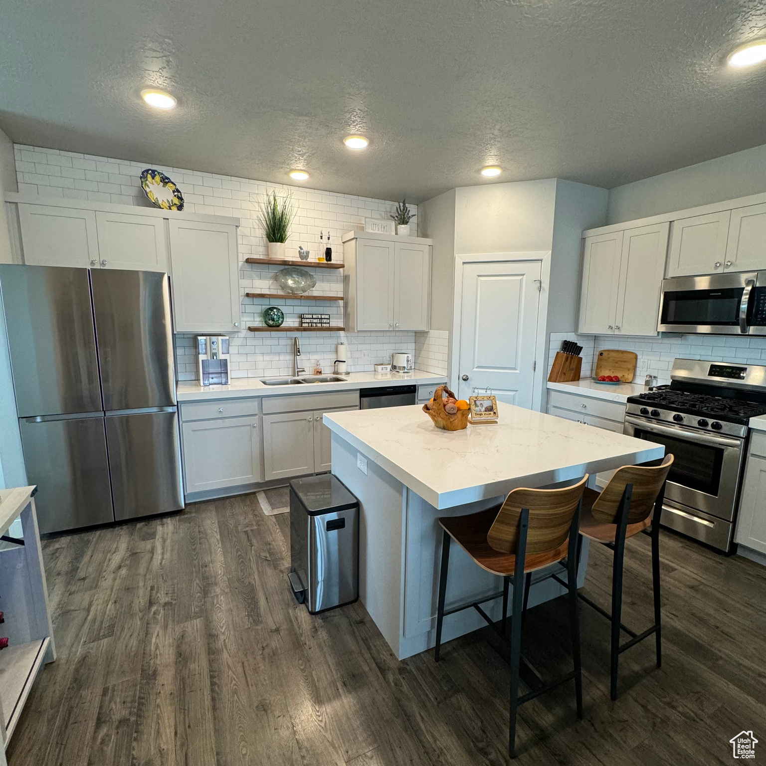 Kitchen with dark hardwood / wood-style flooring, appliances with stainless steel finishes, a center island, and tasteful backsplash