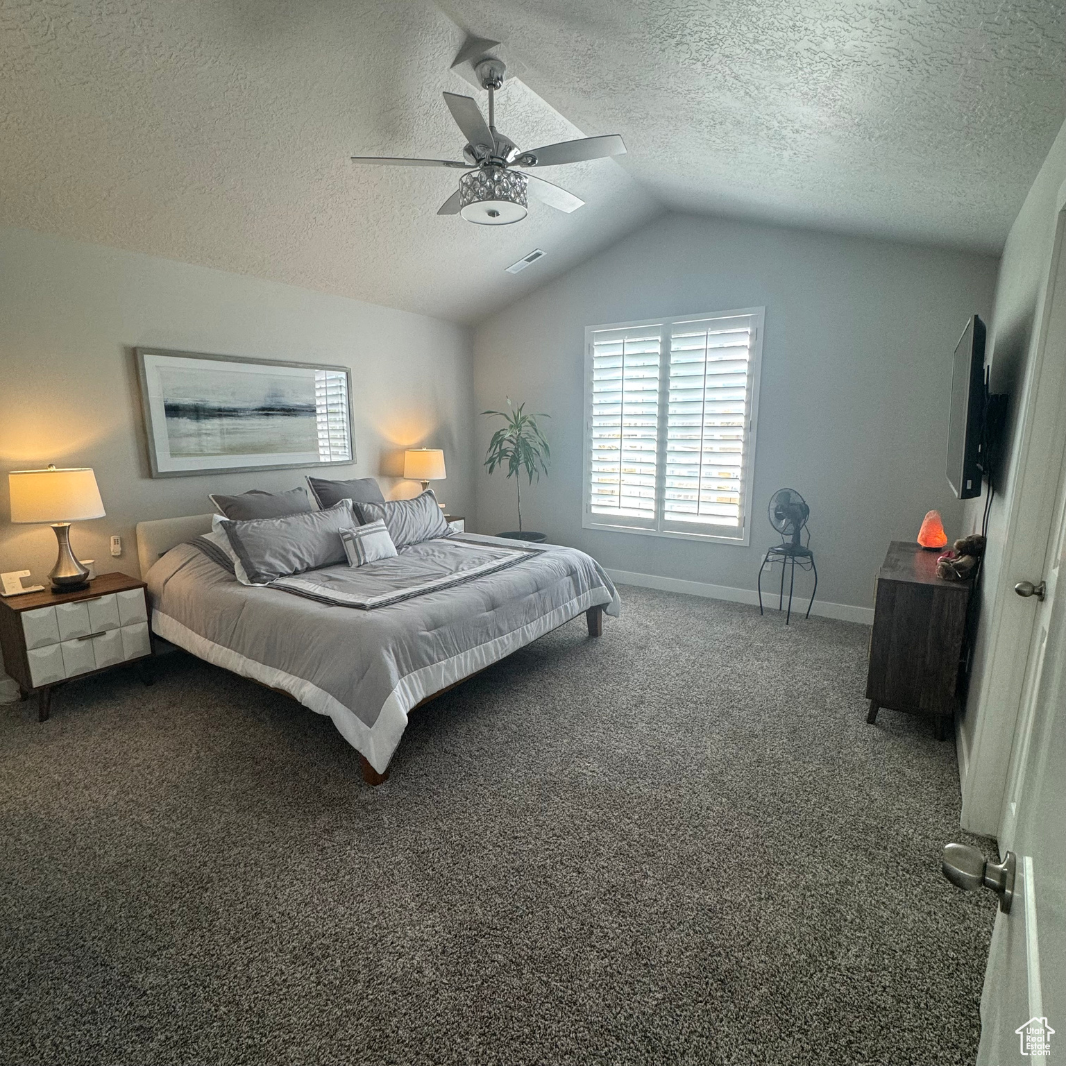 Bedroom featuring a textured ceiling, vaulted ceiling, ceiling fan, and dark colored carpet