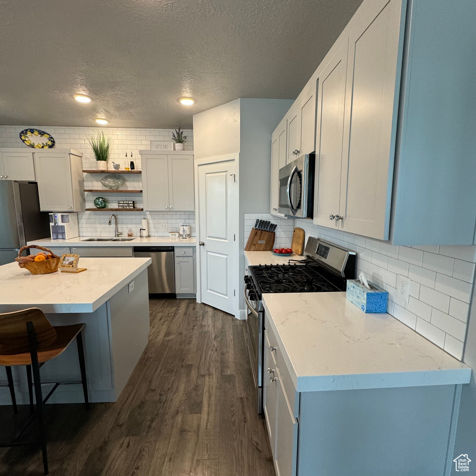 Kitchen with a textured ceiling, sink, backsplash, dark hardwood / wood-style flooring, and stainless steel appliances
