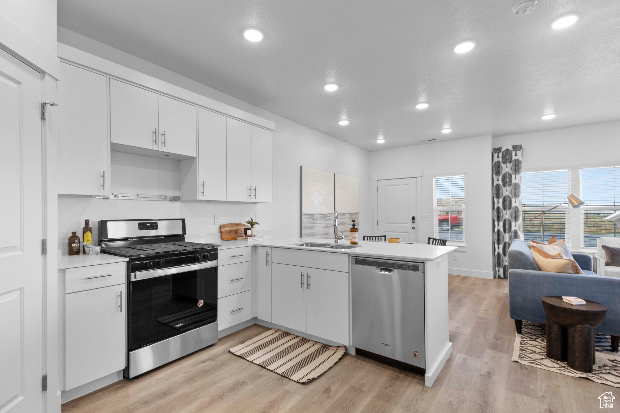 Kitchen with appliances with stainless steel finishes, light hardwood / wood-style flooring, kitchen peninsula, and white cabinets