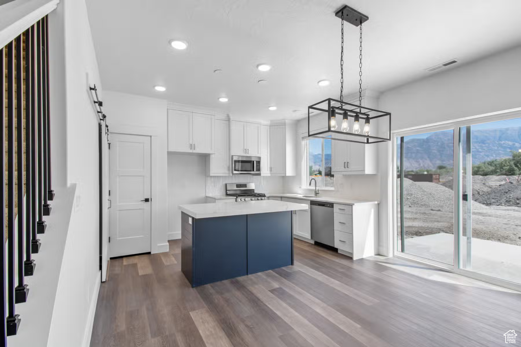 Kitchen with a center island, pendant lighting, white cabinetry, hardwood / wood-style floors, and stainless steel appliances