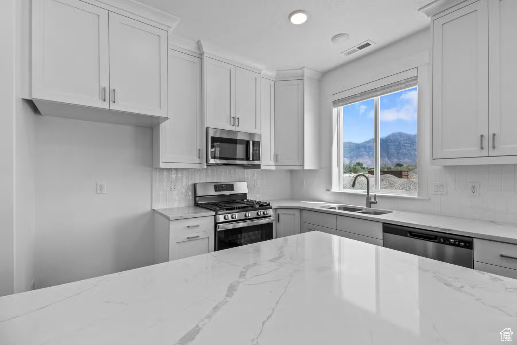 Kitchen featuring appliances with stainless steel finishes, white cabinets, sink, and light stone countertops