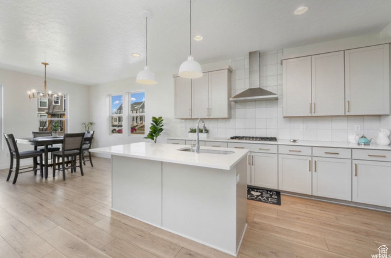 Kitchen featuring hanging light fixtures, light hardwood / wood-style floors, wall chimney range hood, and tasteful backsplash