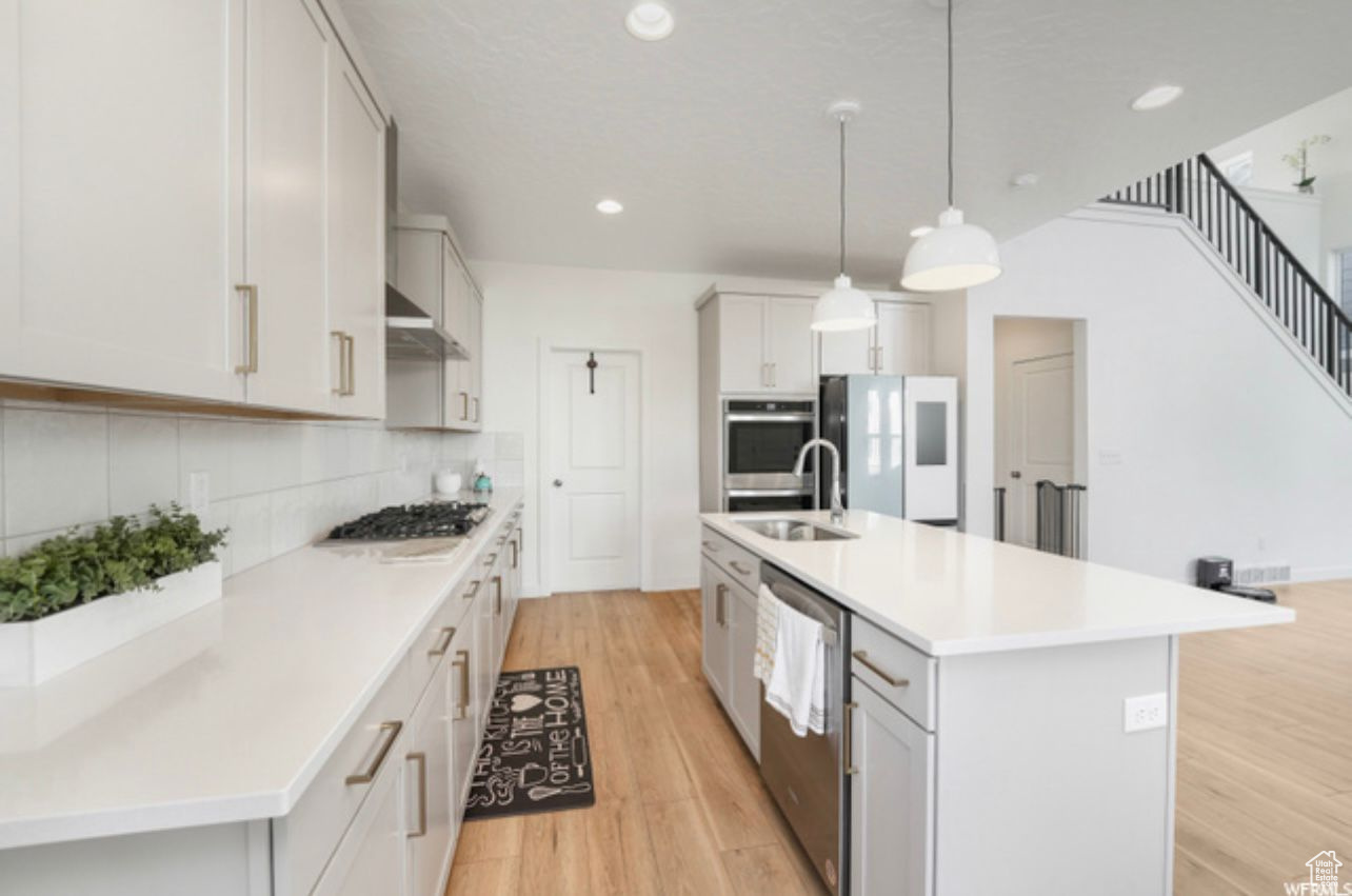 Kitchen with backsplash, stainless steel appliances, an island with sink, sink, and light wood-type flooring