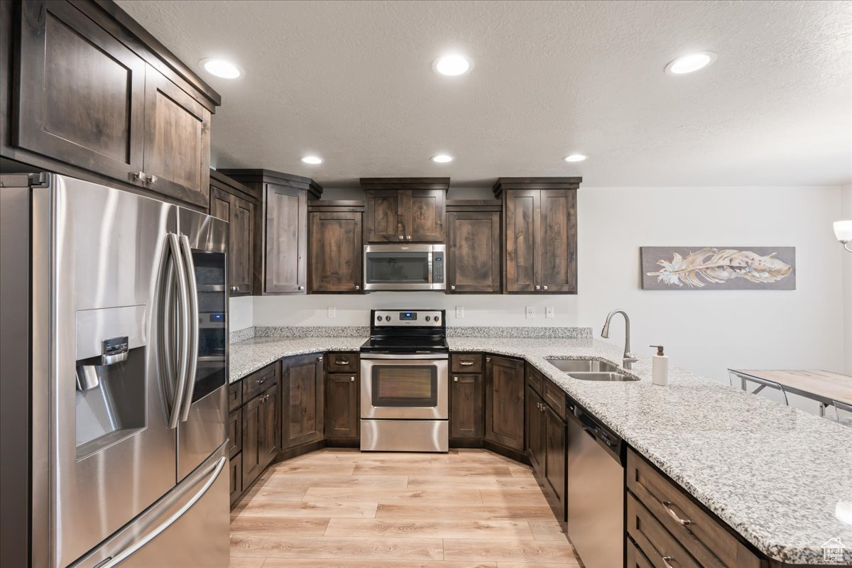 Kitchen with light stone countertops, kitchen peninsula, appliances with stainless steel finishes, light laminate plank floors, and sink