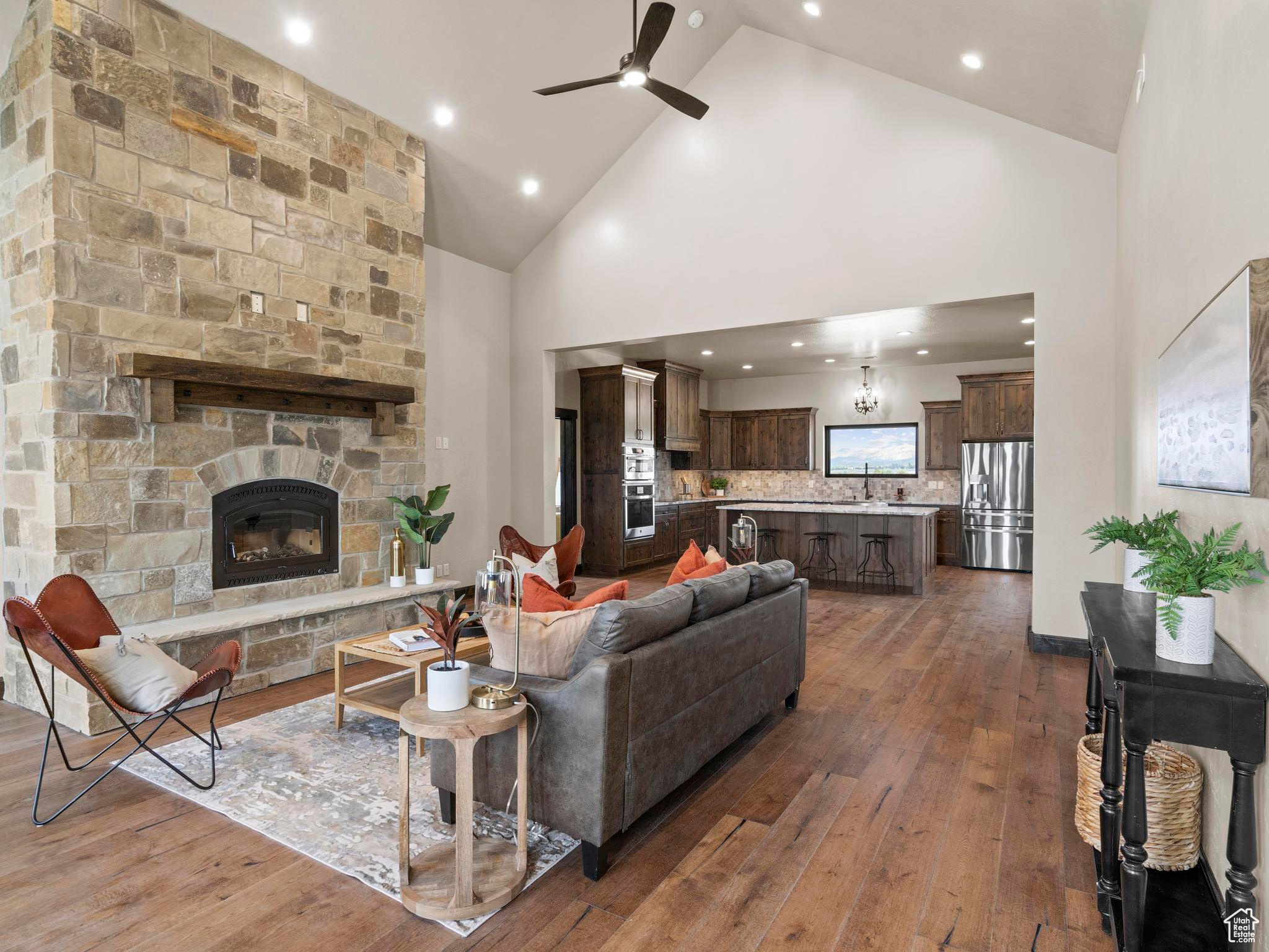 Great room with a real stone fireplace, high vaulted ceiling, ceiling fan, and real wood floors