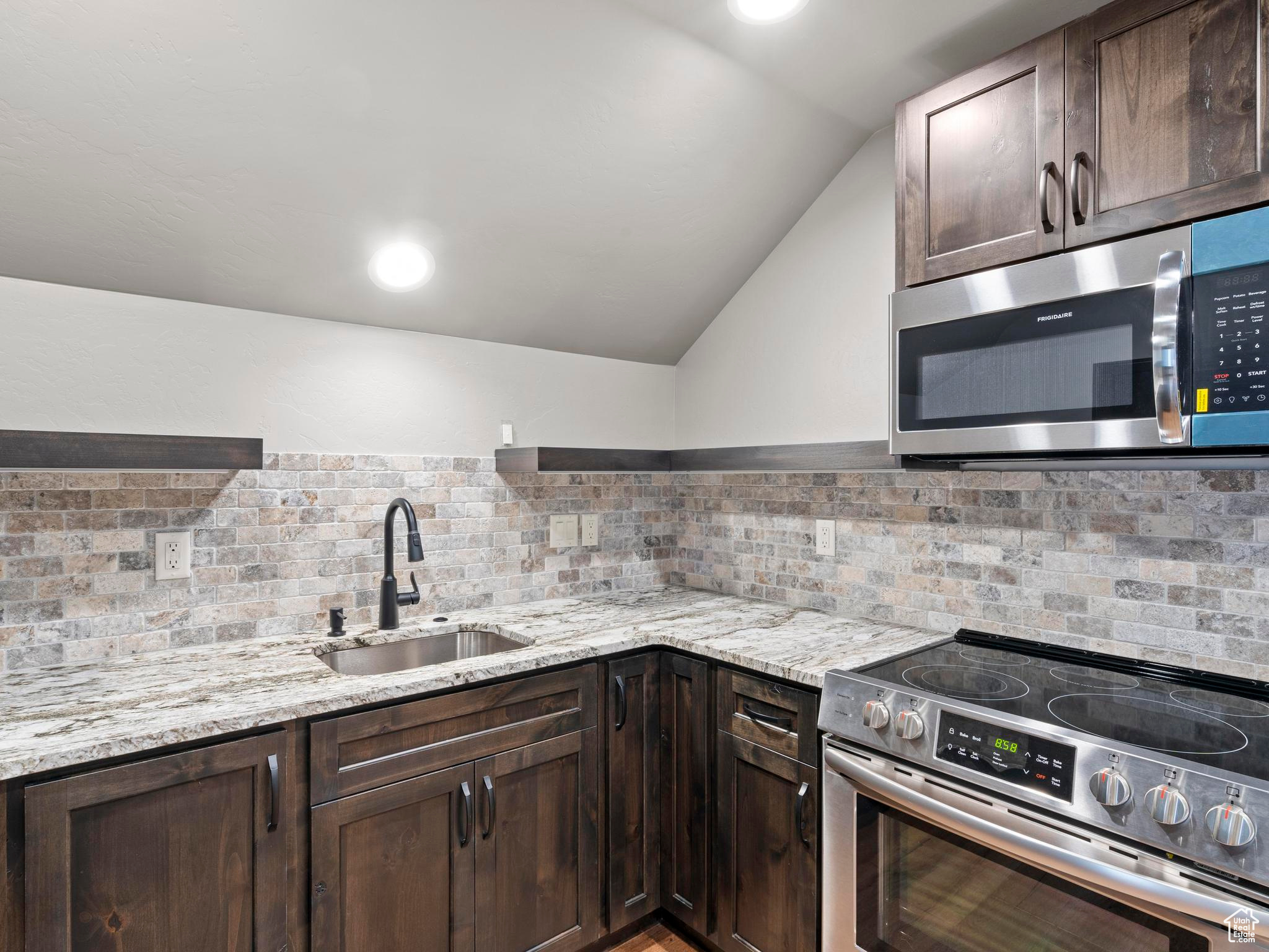 Fully equiped accessory Kitchen featuring lofted ceiling, stainless steel appliances custom backsplash.