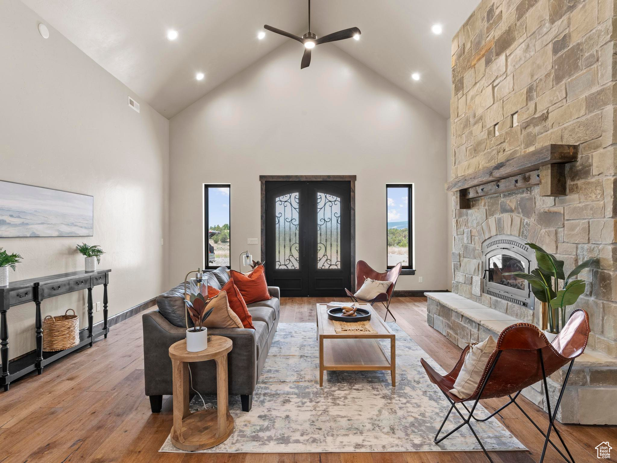 Great room with a realstone fireplace, high vaulted ceiling, ceiling fan, and real wood floors